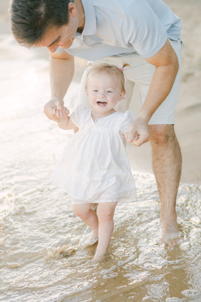 baby girl laughs as she steps in the surf at the beach