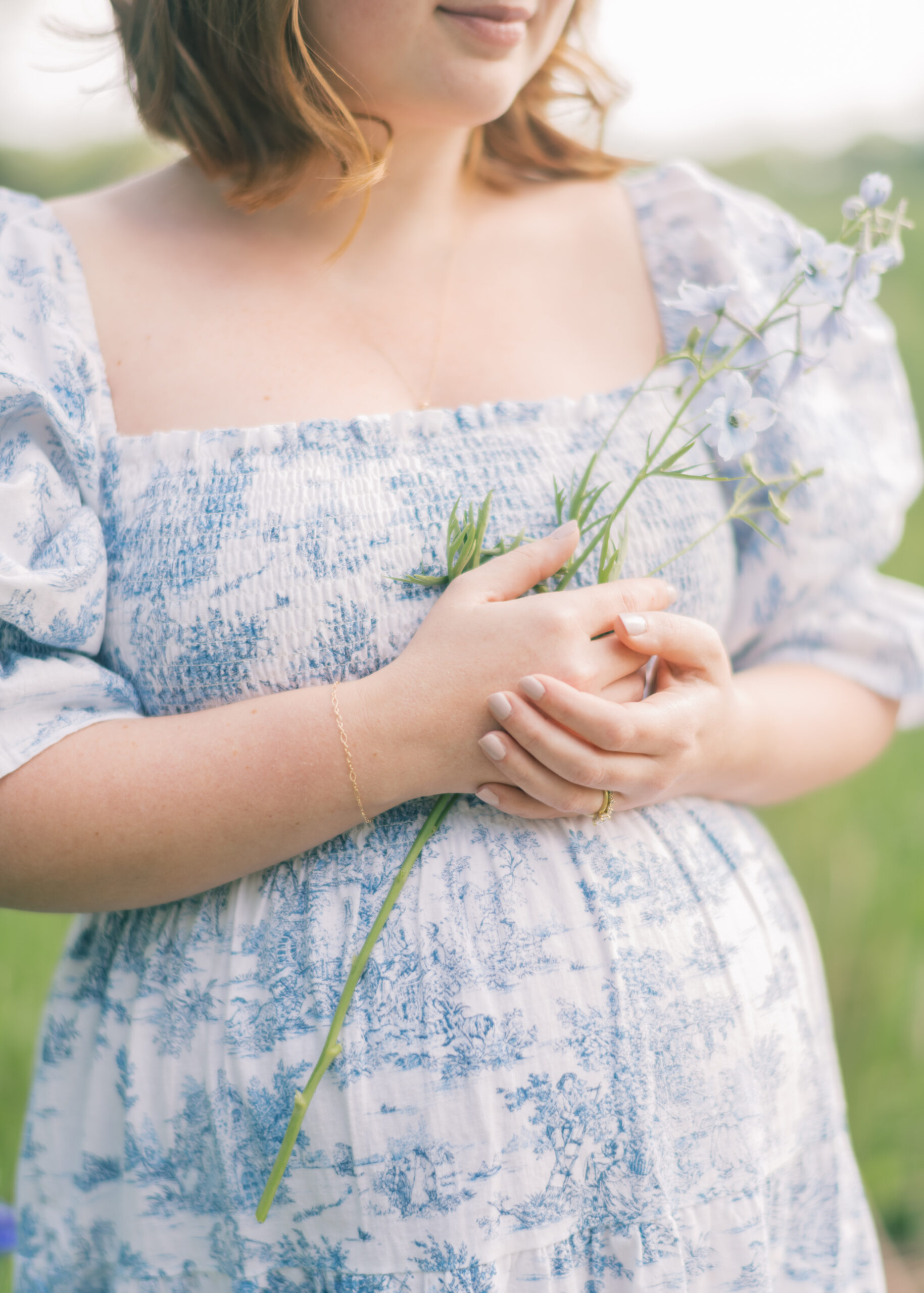 a pregnant woman stands holding a sprig of florals against her bump