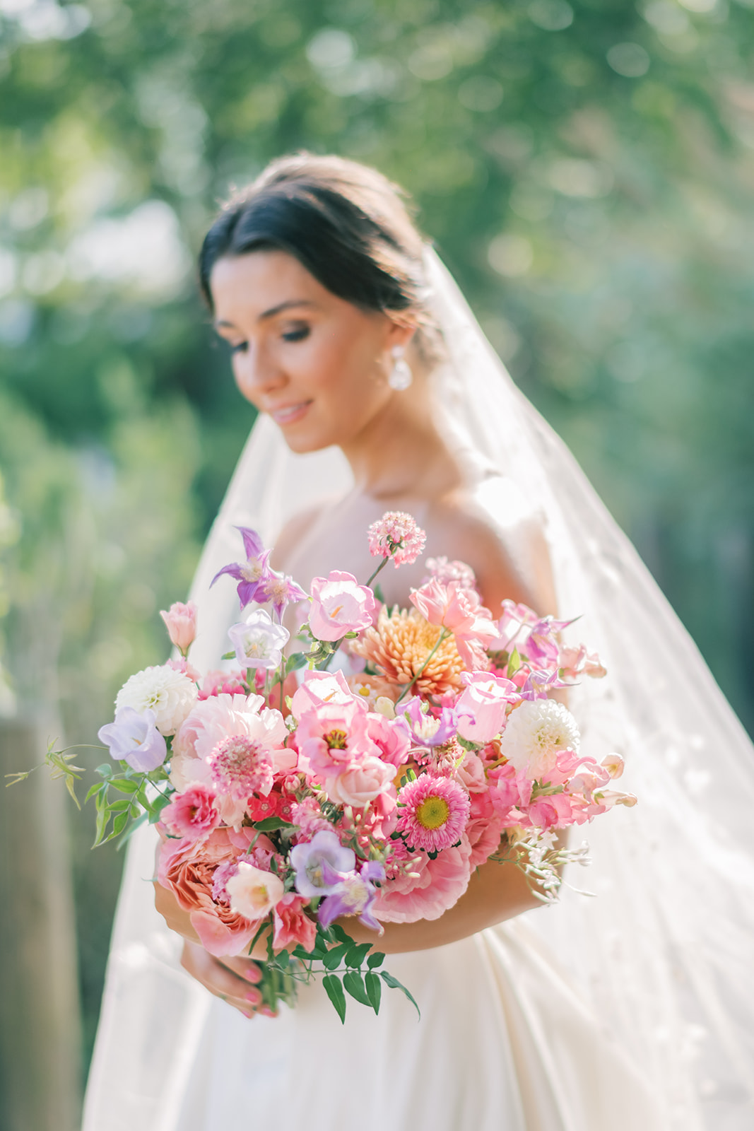 bride holds pink and purple bouquet with veil round the shoulder