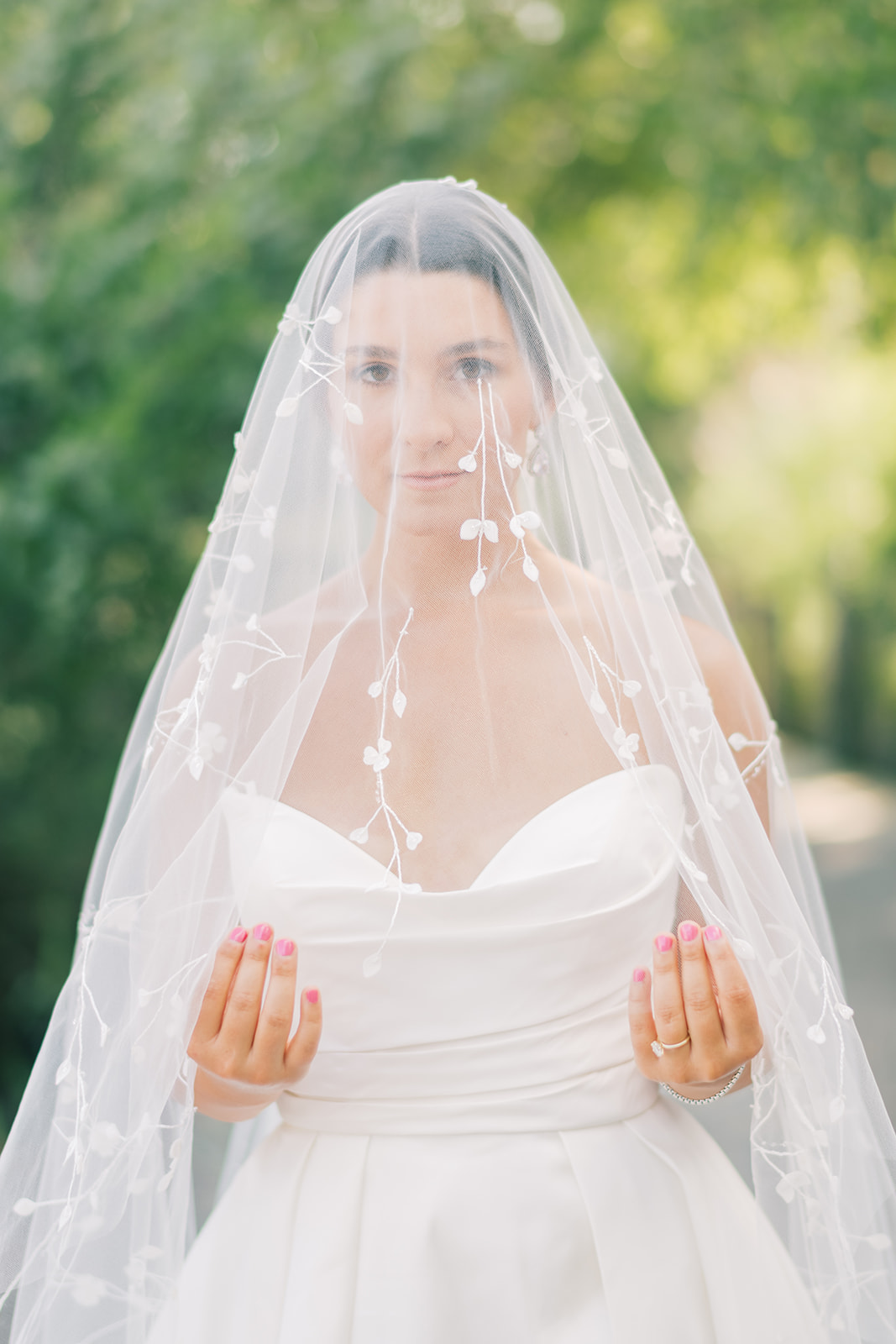 bride pulls veil with flower accents around shoulders and in front of her
