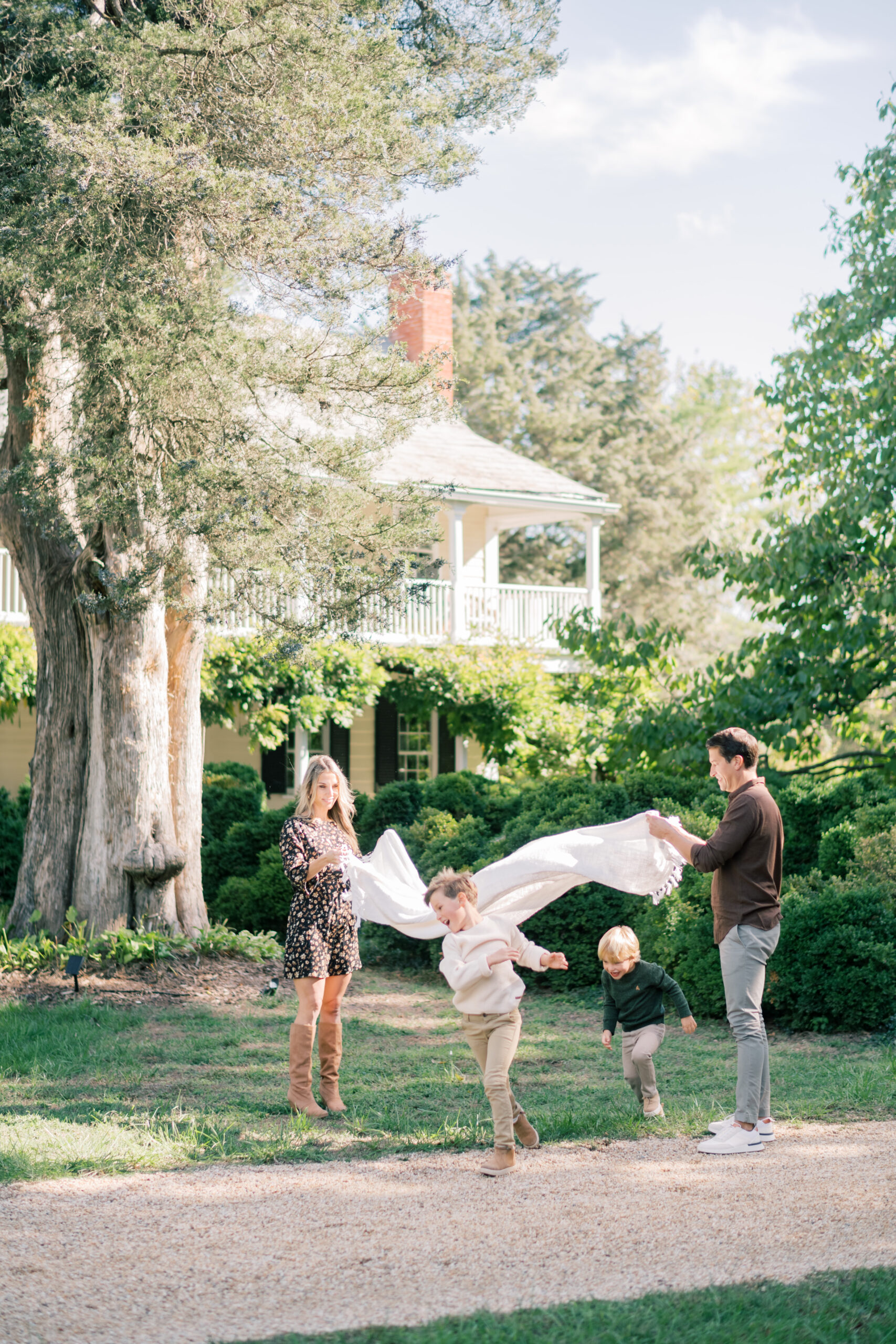 parents play with blanket while kids run under it in front of home during Southern Maryland family portraits
