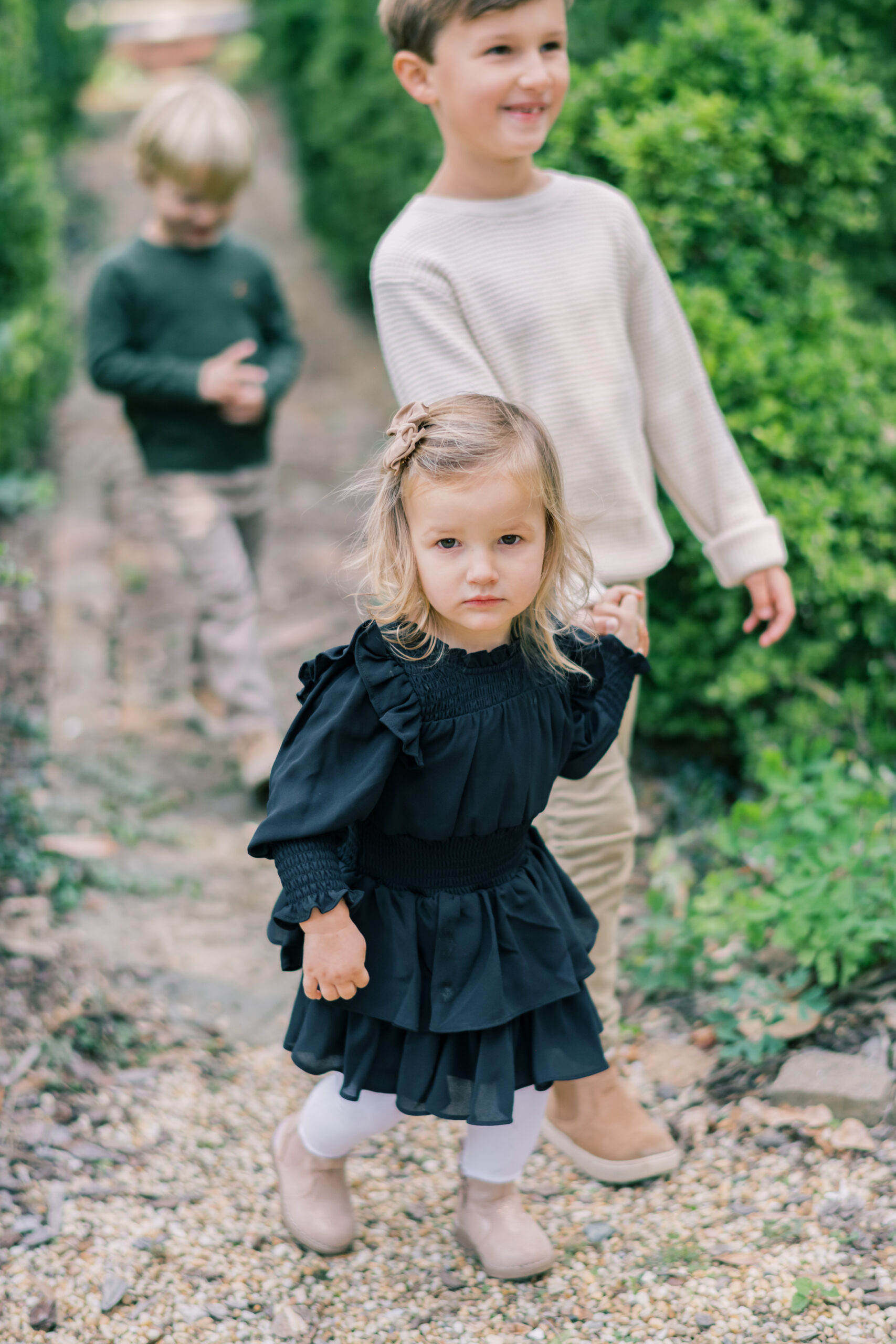 little girl in emerald green dress holds hands with big brother in white sweater during fall family photos 