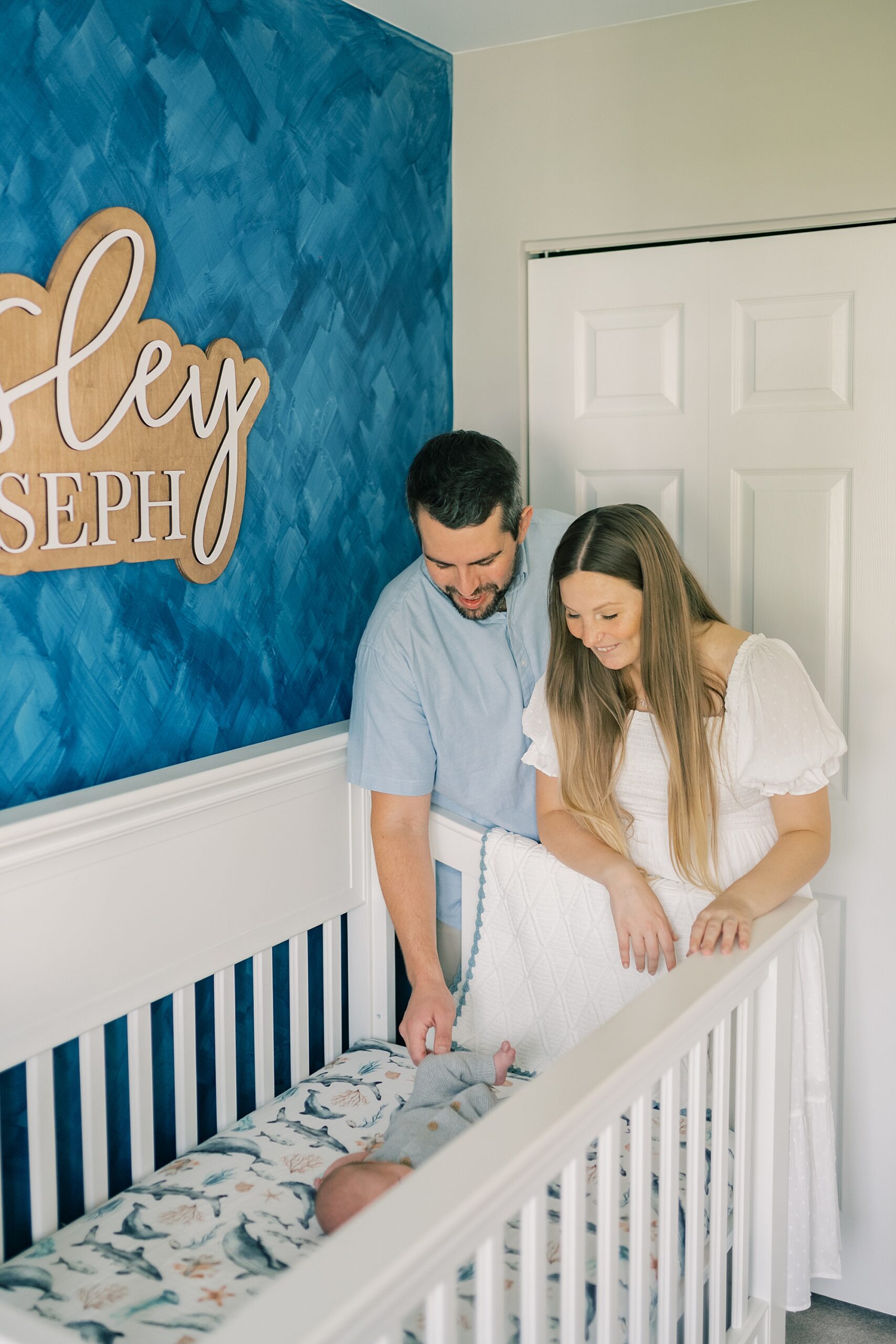 parents look over edge of crib at baby boy during Annapolis lifestyle newborn session at home in nautical nursery