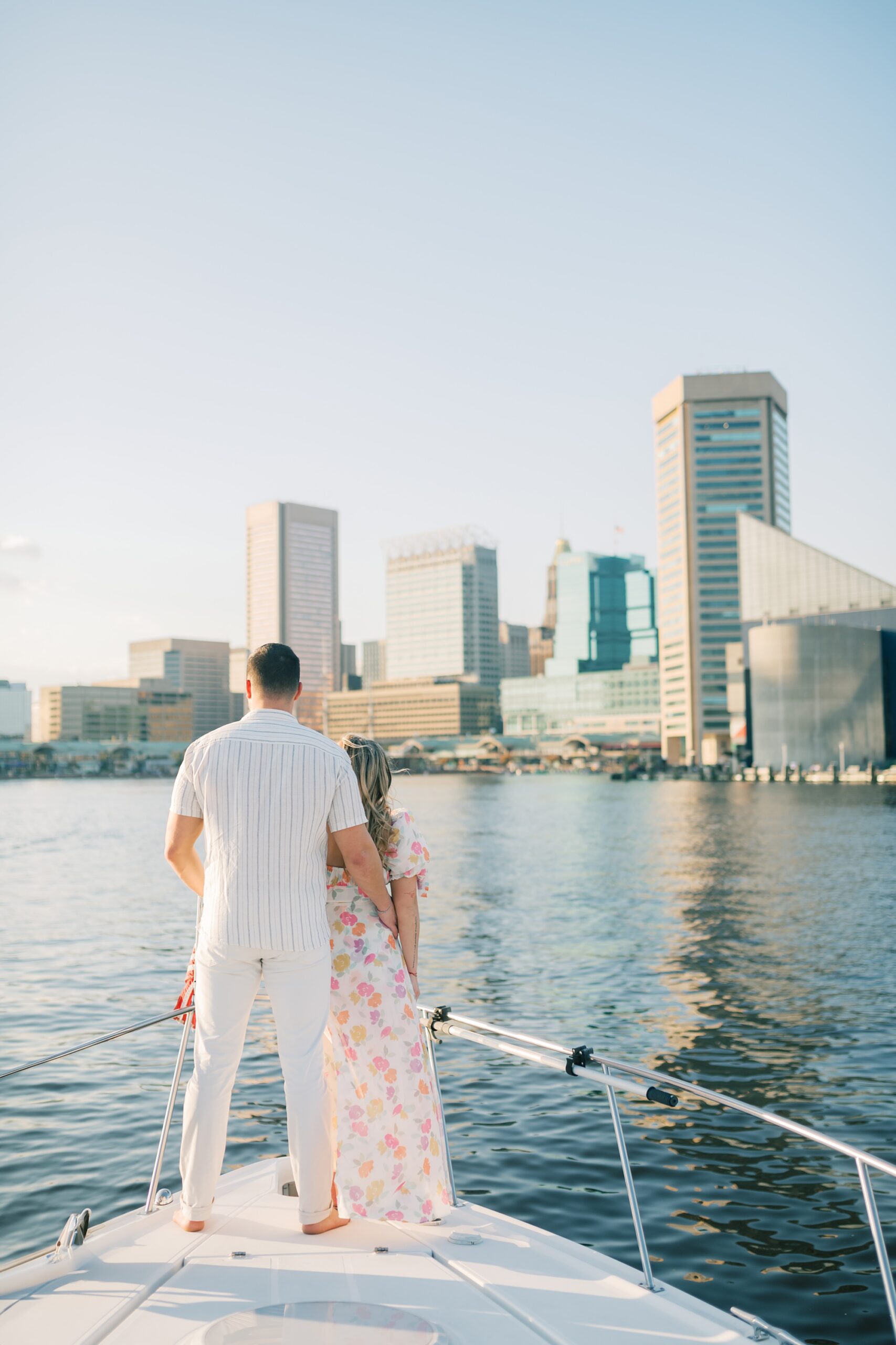man holds woman's waist standing on front of boat sailing around the Inner Harbor in Baltimore MD