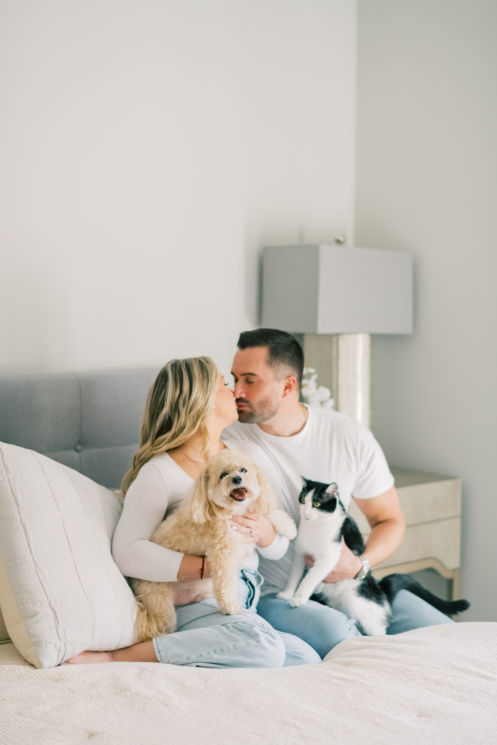 engaged couple sits on bed with cat and dog in their lap