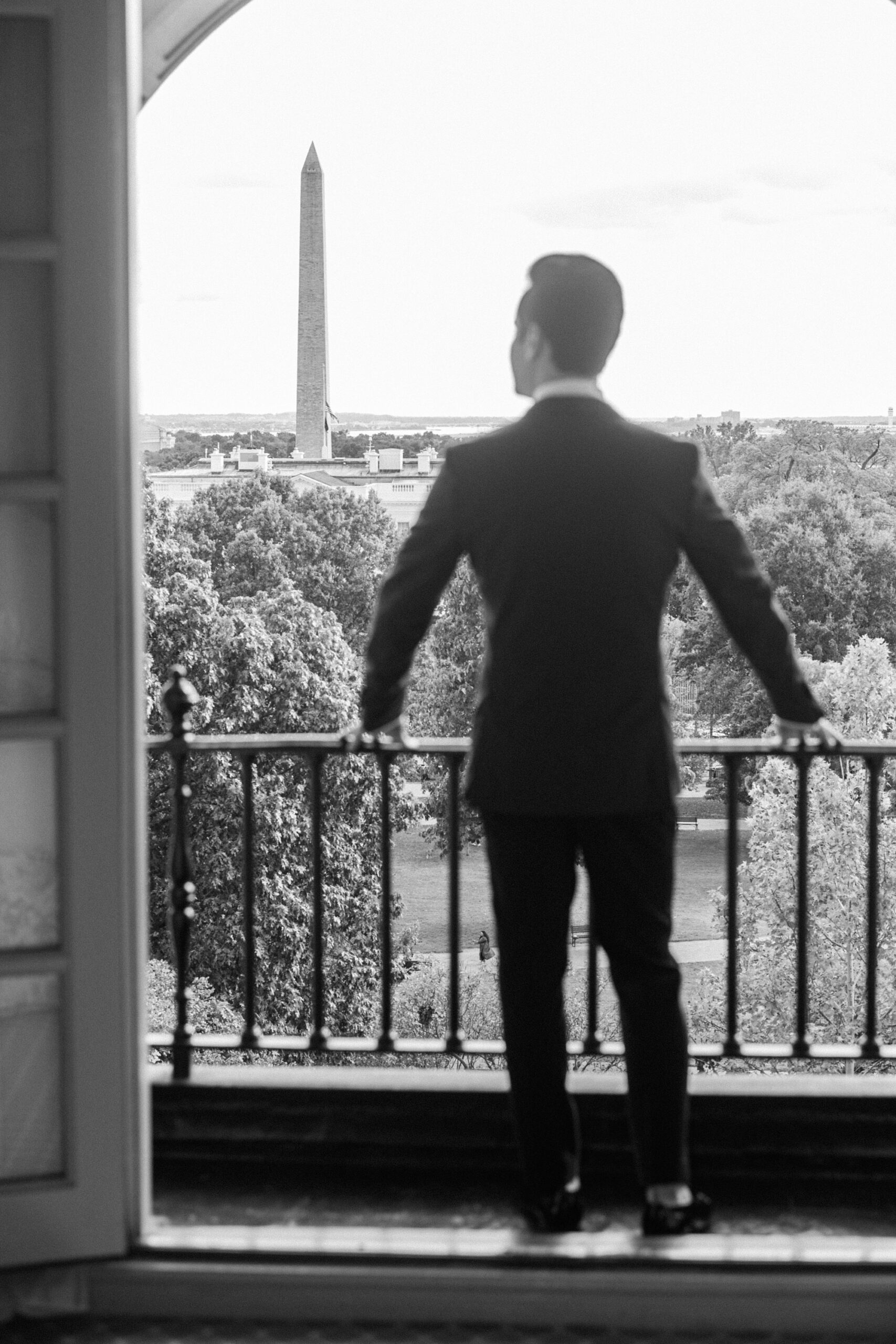 groom stands on balcony looking over DC from the Hay Adams Hotel