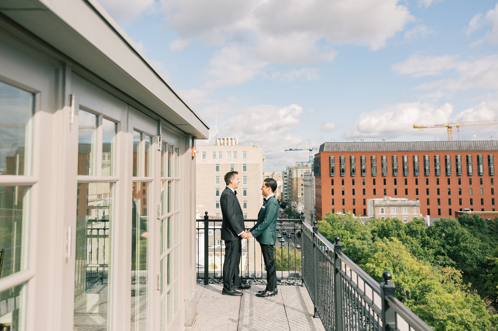 grooms pose on balcony holding hands overlooking Washington DC
