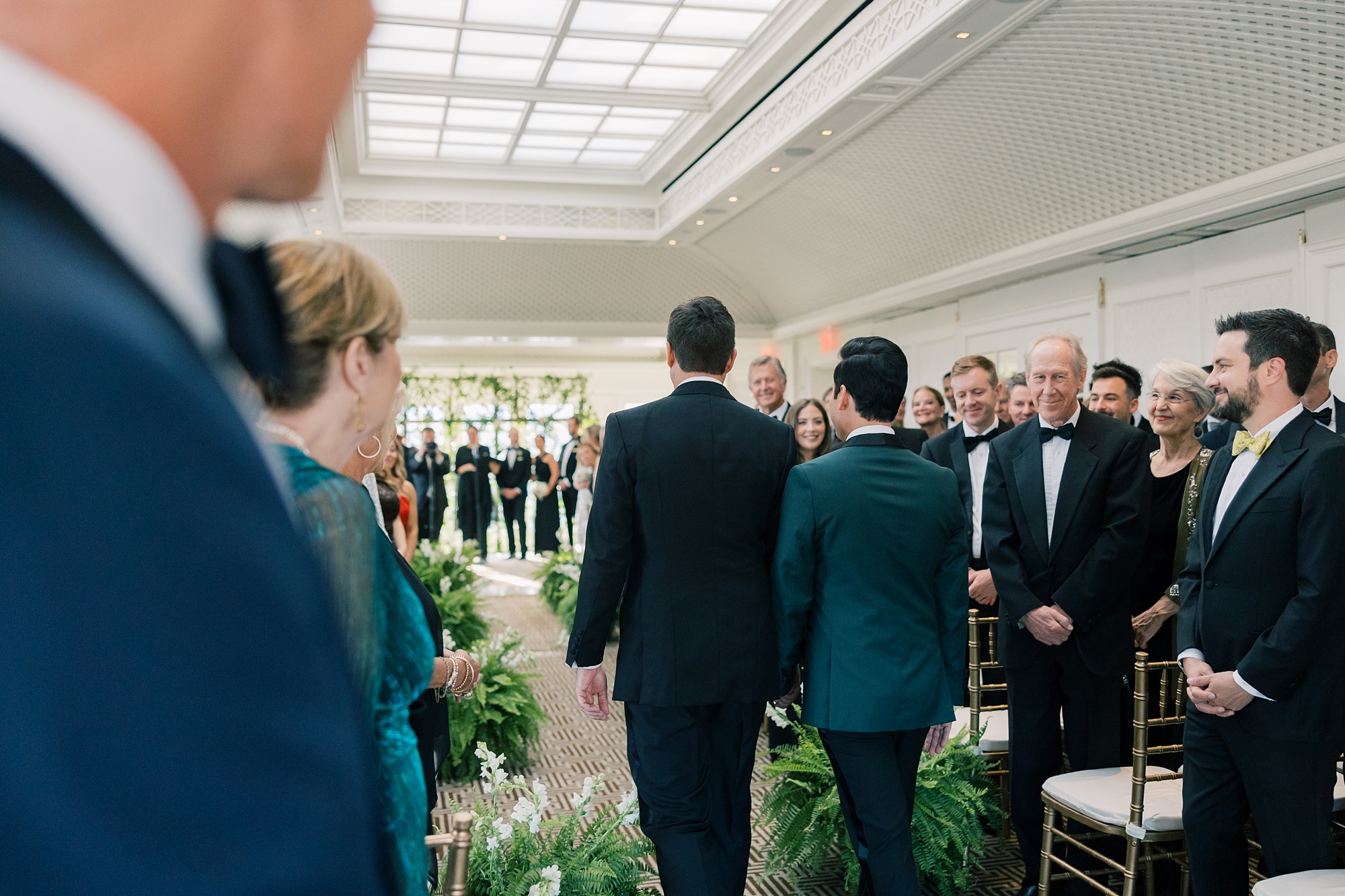 grooms hold hands walking down aisle for ceremony together 