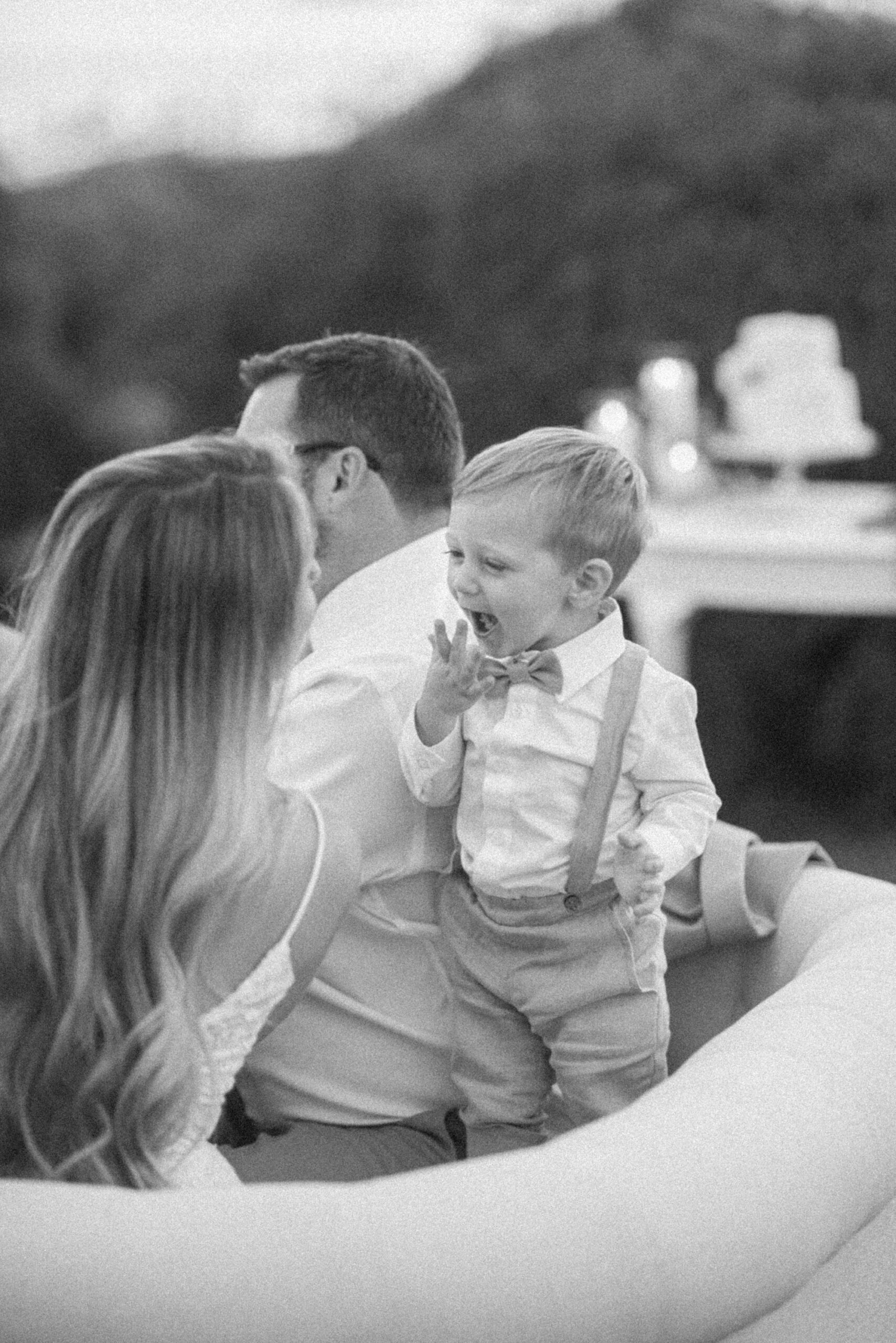 toddler laughs on back of sofa with bride during al fresco wedding reception at Rousby Hall