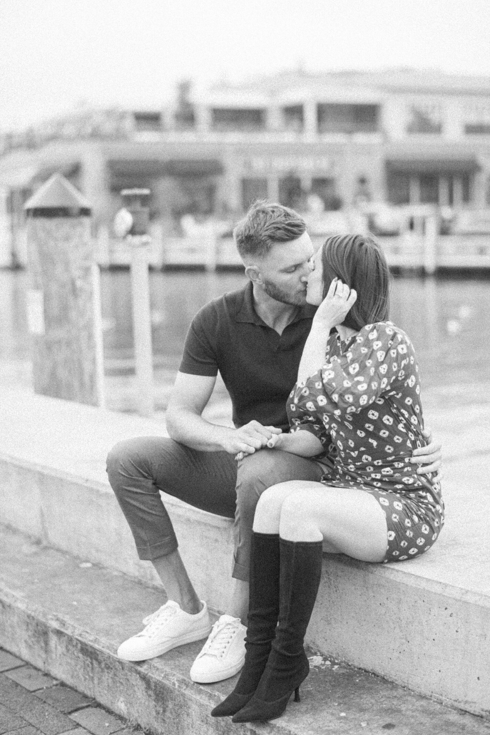 engaged couple sits on wall in front of Downtown Annapolis waterfront