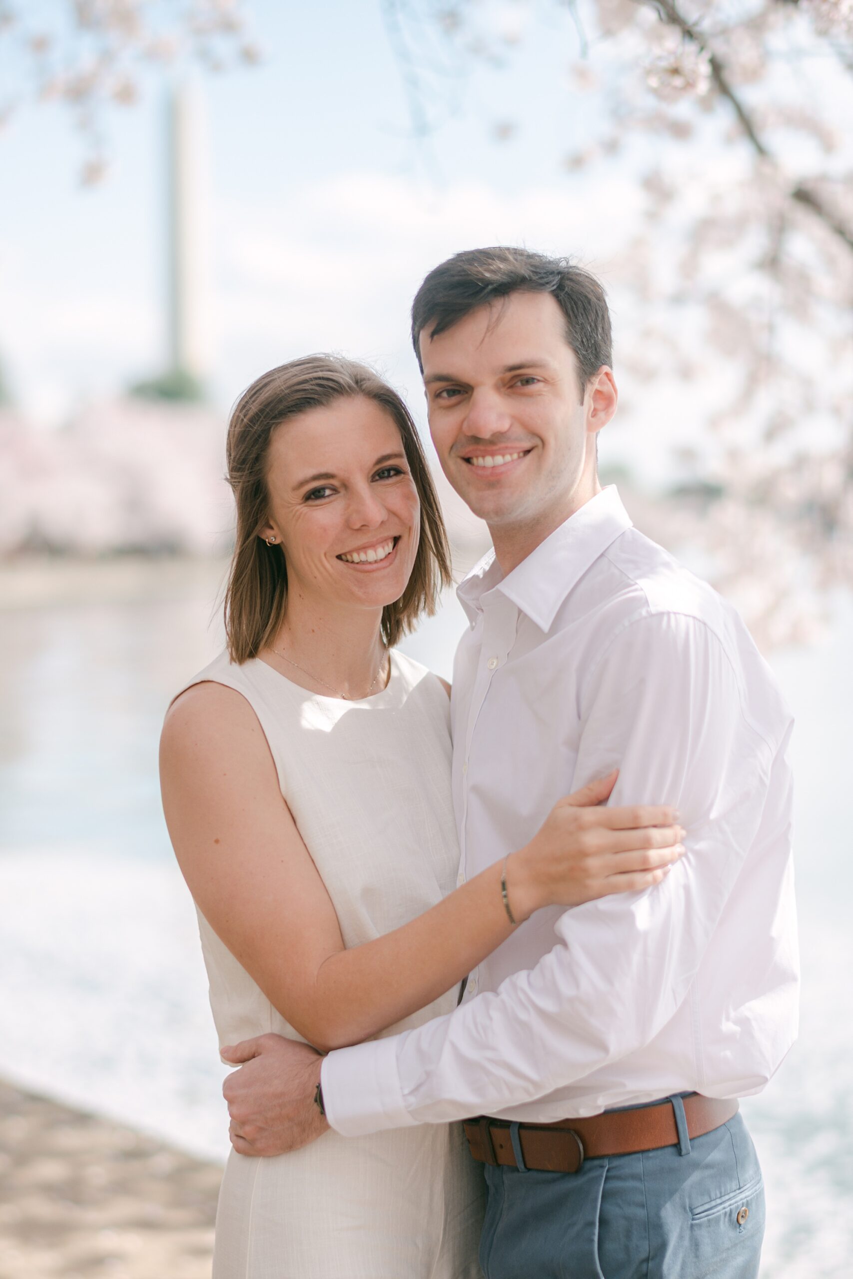 man and woman hug in front of Washington Monument during DC cherry blossom engagement photos