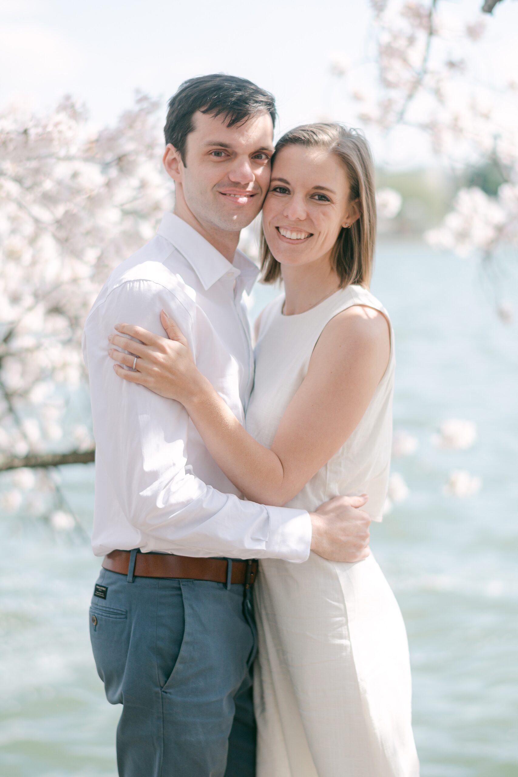 engaged couple hugs in front of cherry blossoms in the Tidal Basin