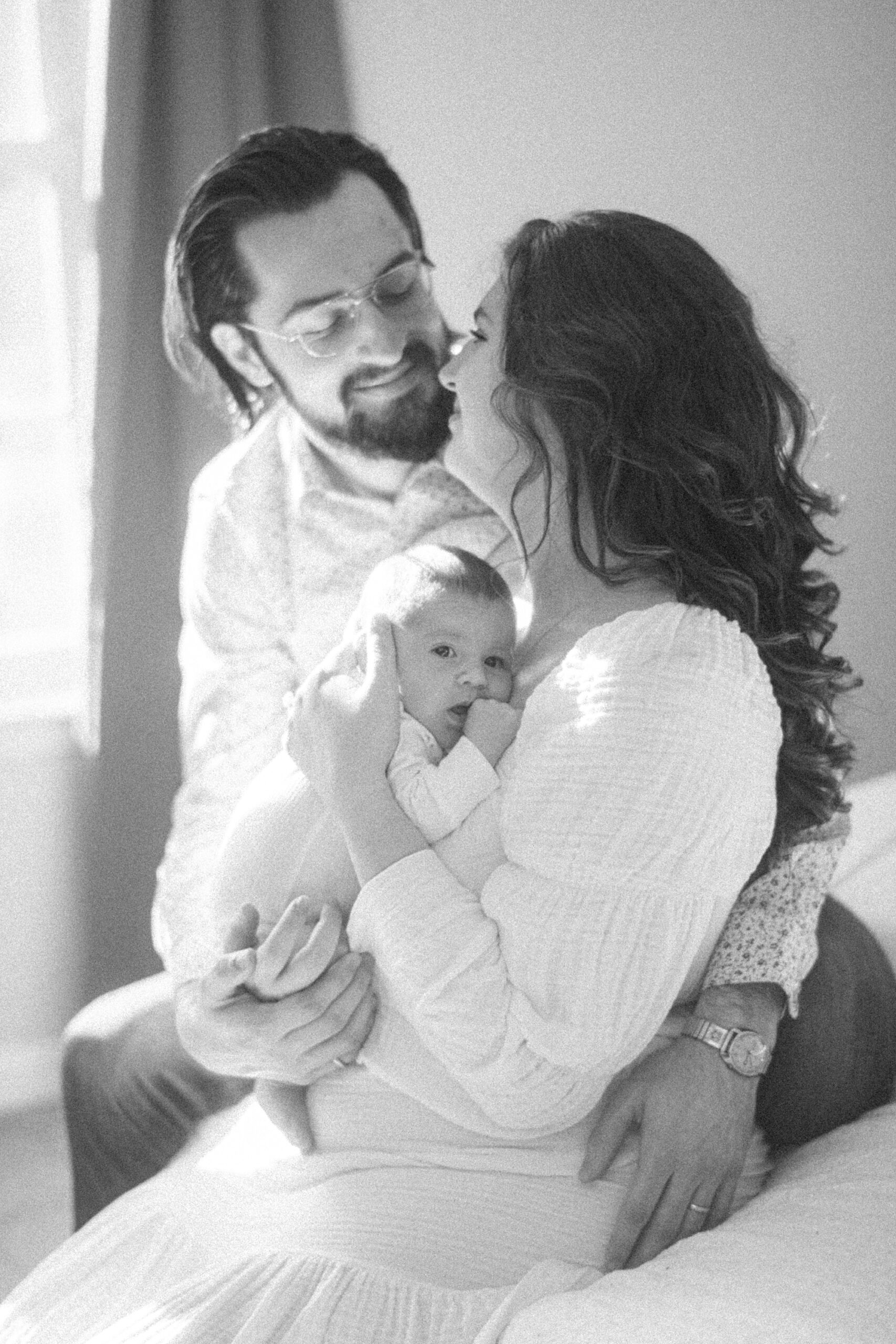 parents lean together holding baby girl on chest during MD lifestyle newborn portraits