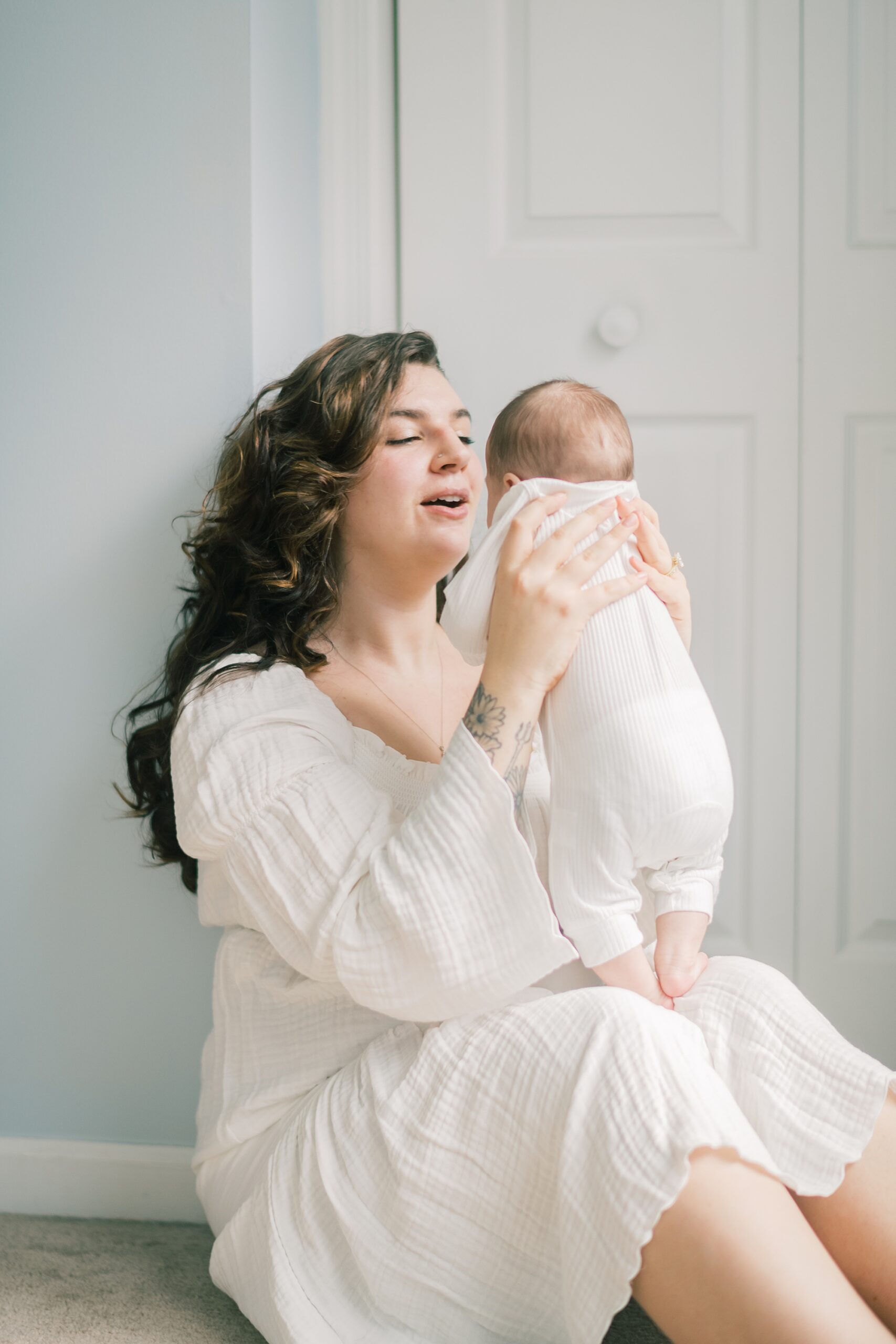 mother lifts up daughter in front of her by door of nursery during lifestyle newborn portraits
