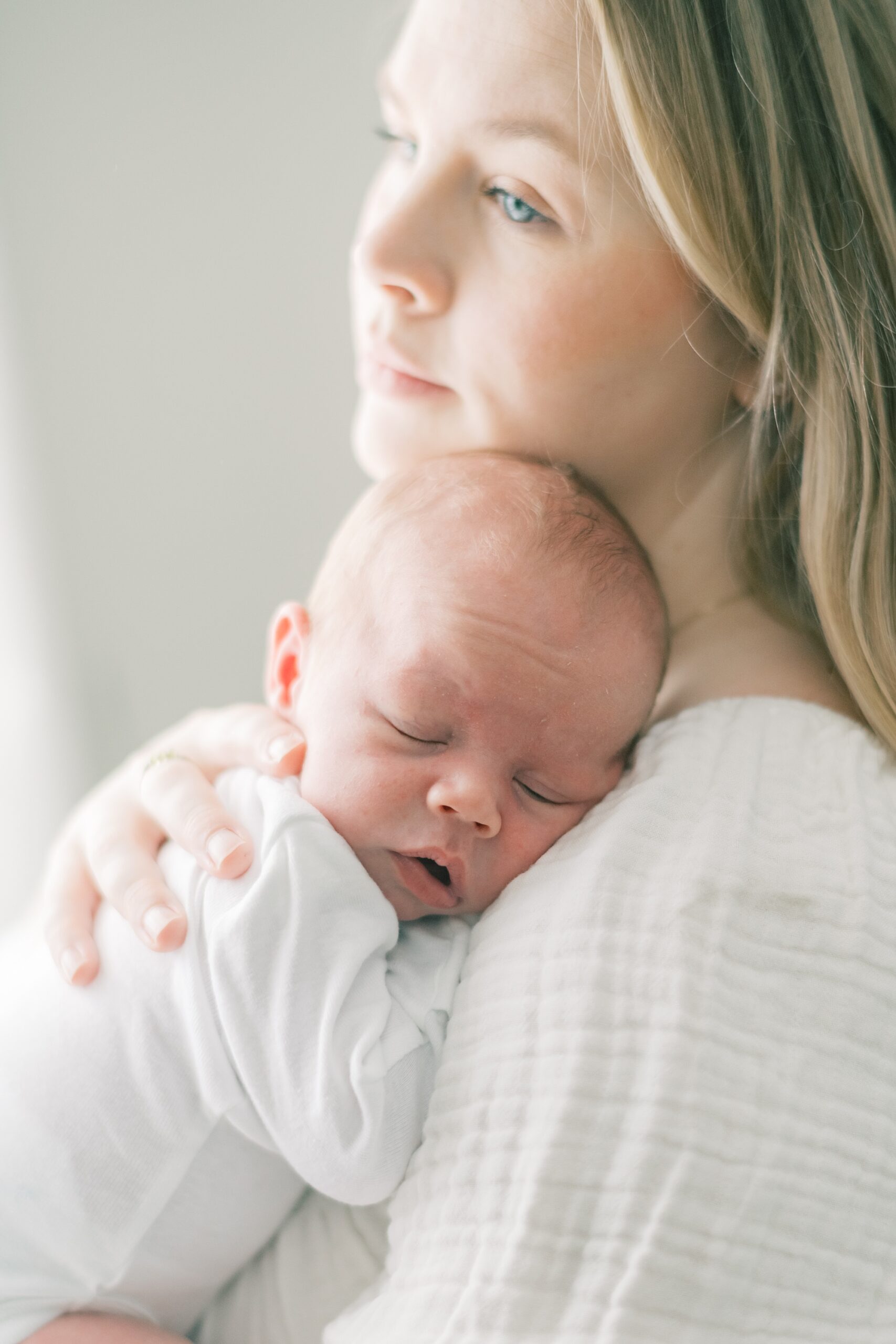 mom holds son on shoulder during in-home newborn portraits