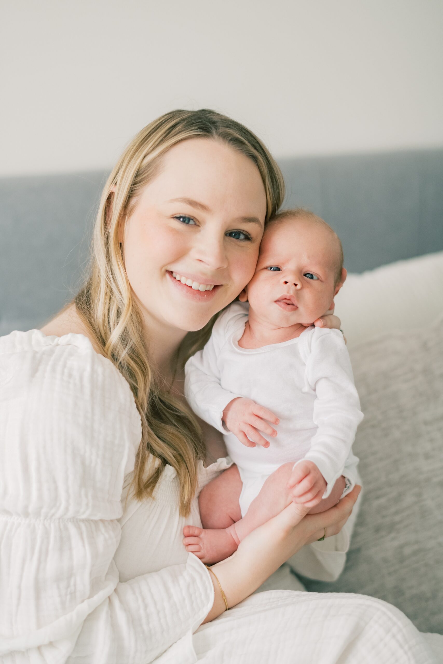 mom holds newborn son against cheek in white onesie during in-home newborn portraits