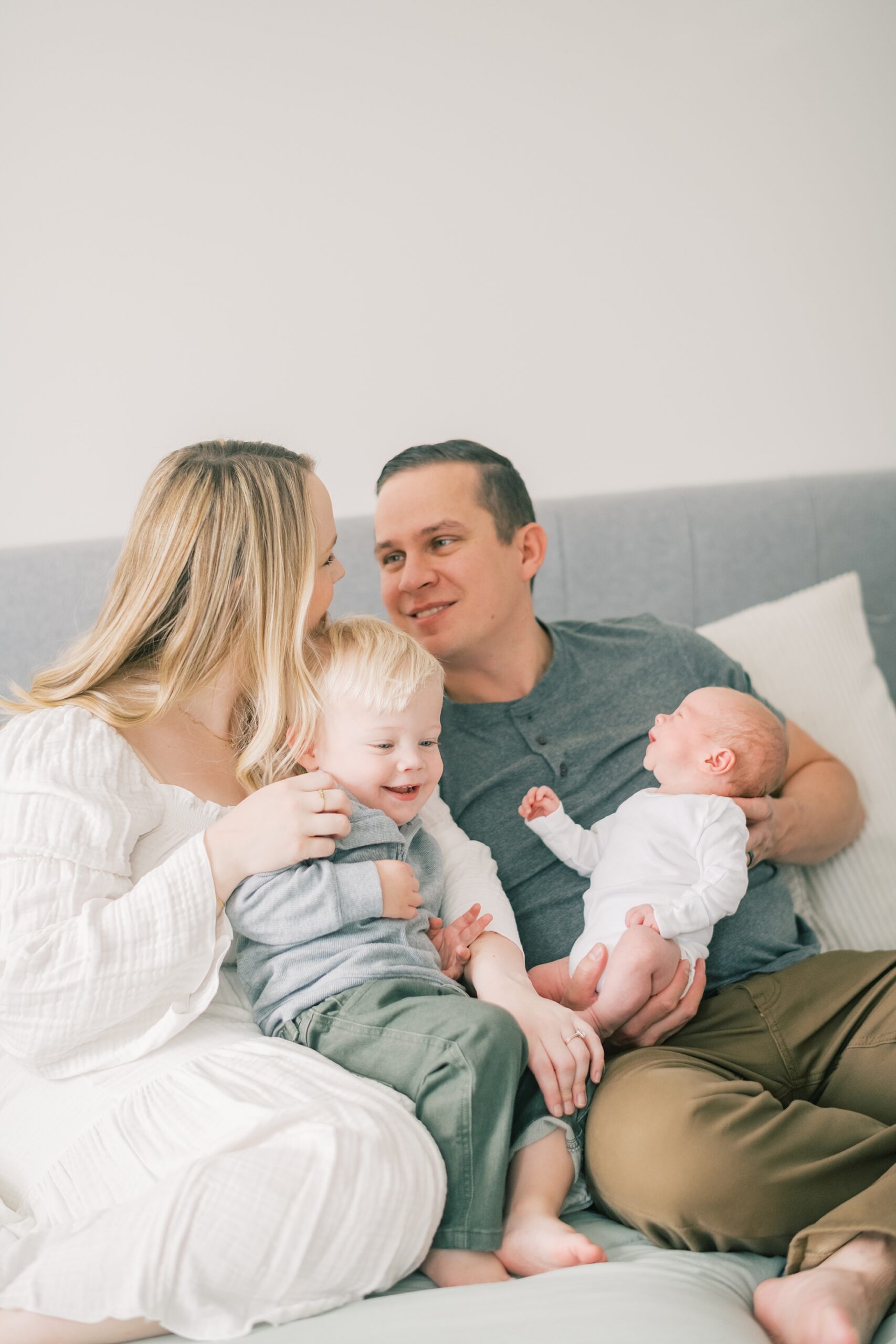 parents smile while holding two boys on bed during in-home newborn portraits