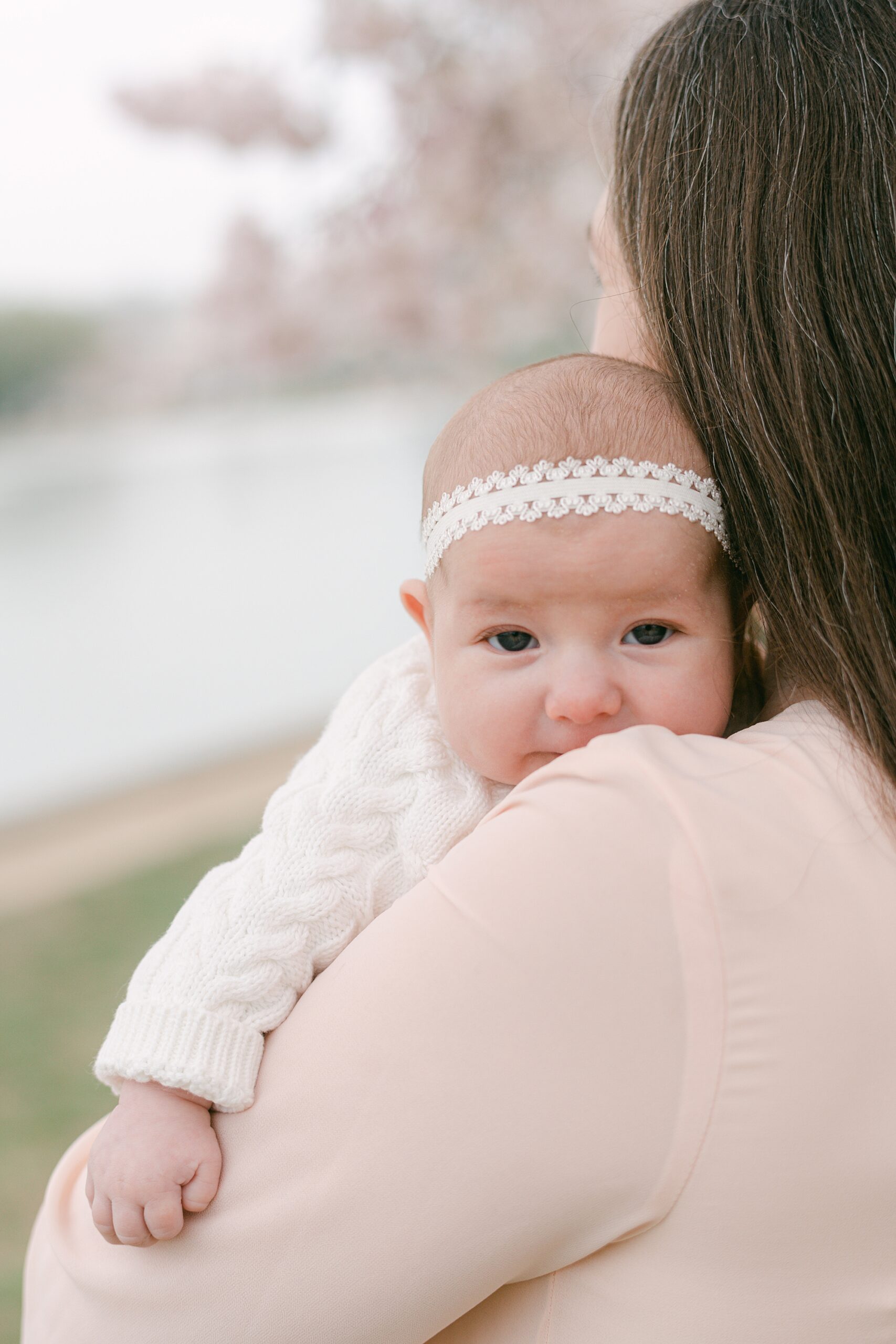 baby girl lays on mom's shoulder with white headband and sweater 