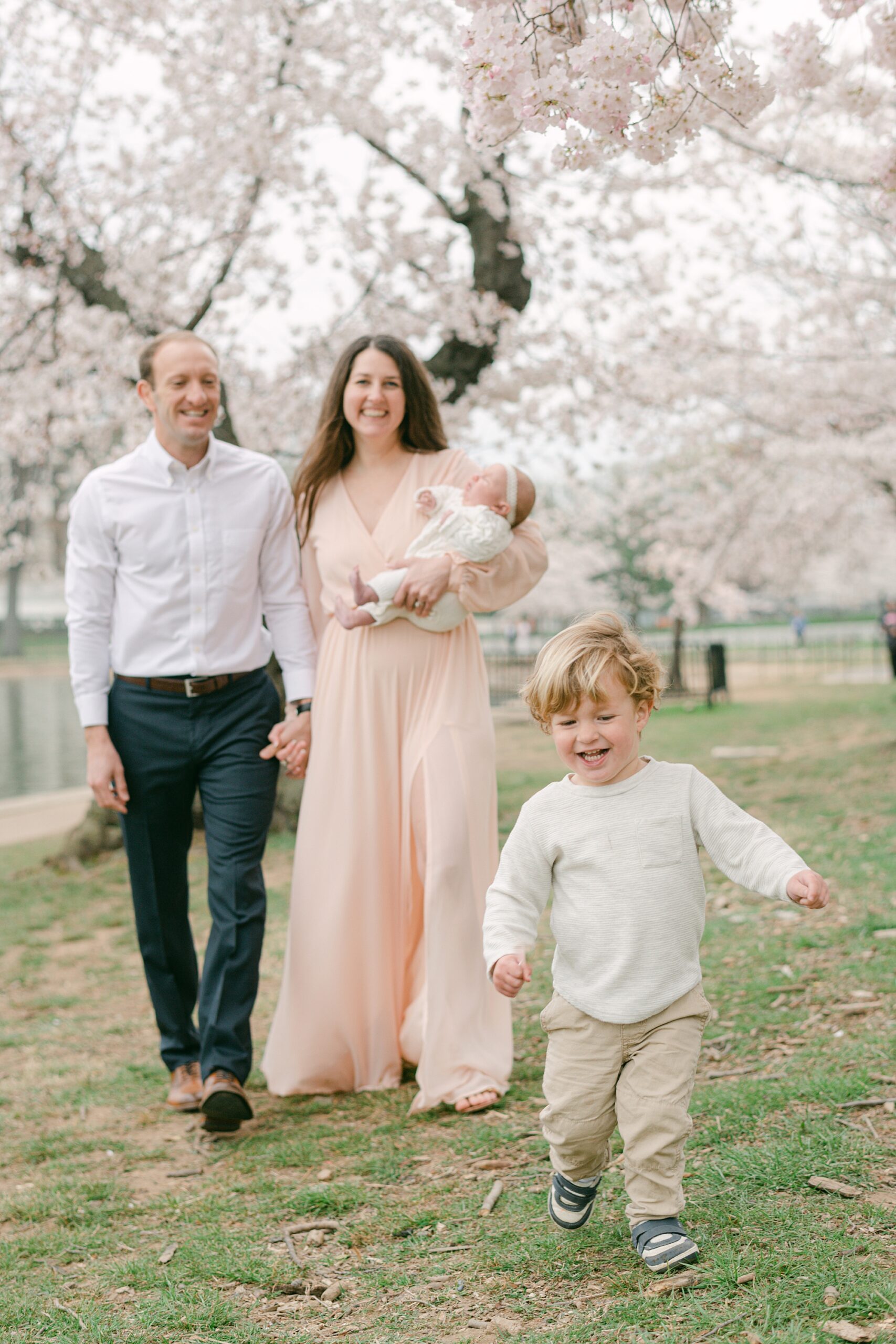 couple holds hands while mom carries baby and toddler runs in front of them during spring photos in DC