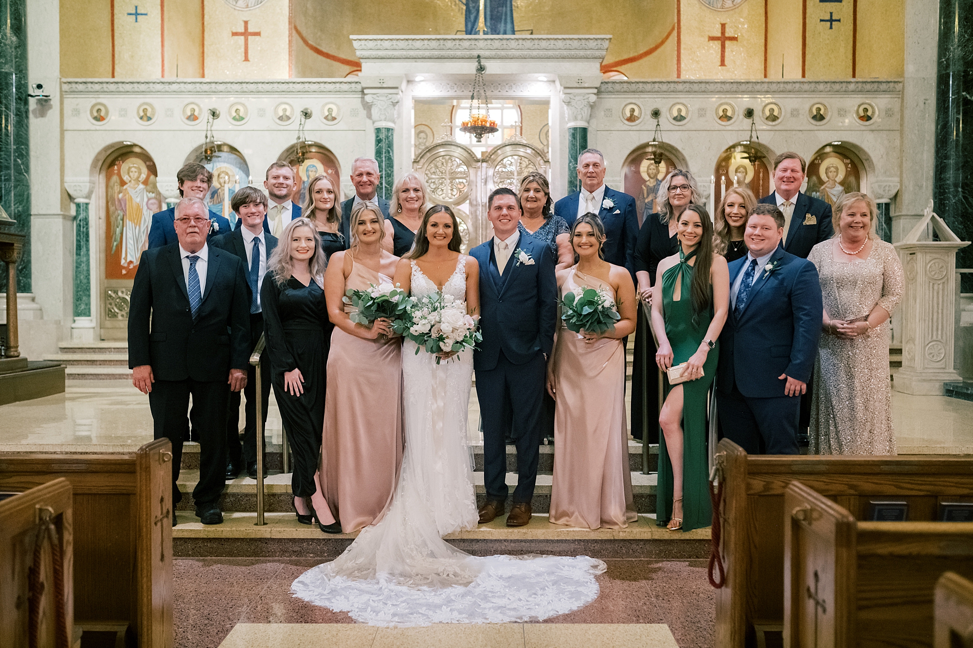bride and groom pose with family inside Greek Orthodox church 