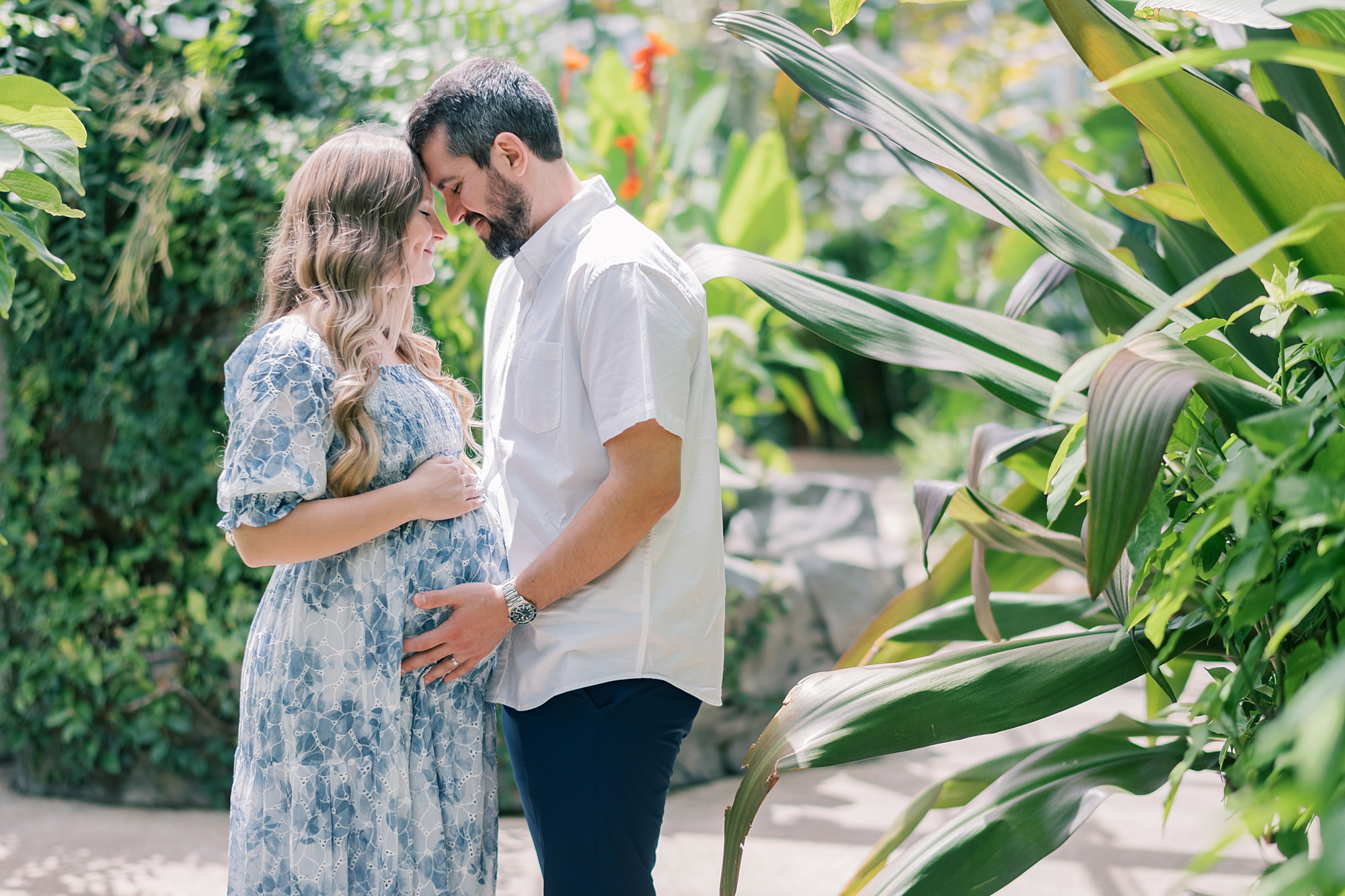 man holds wife's belly in blue and white gown during Rawlings Conservatory maternity portraits