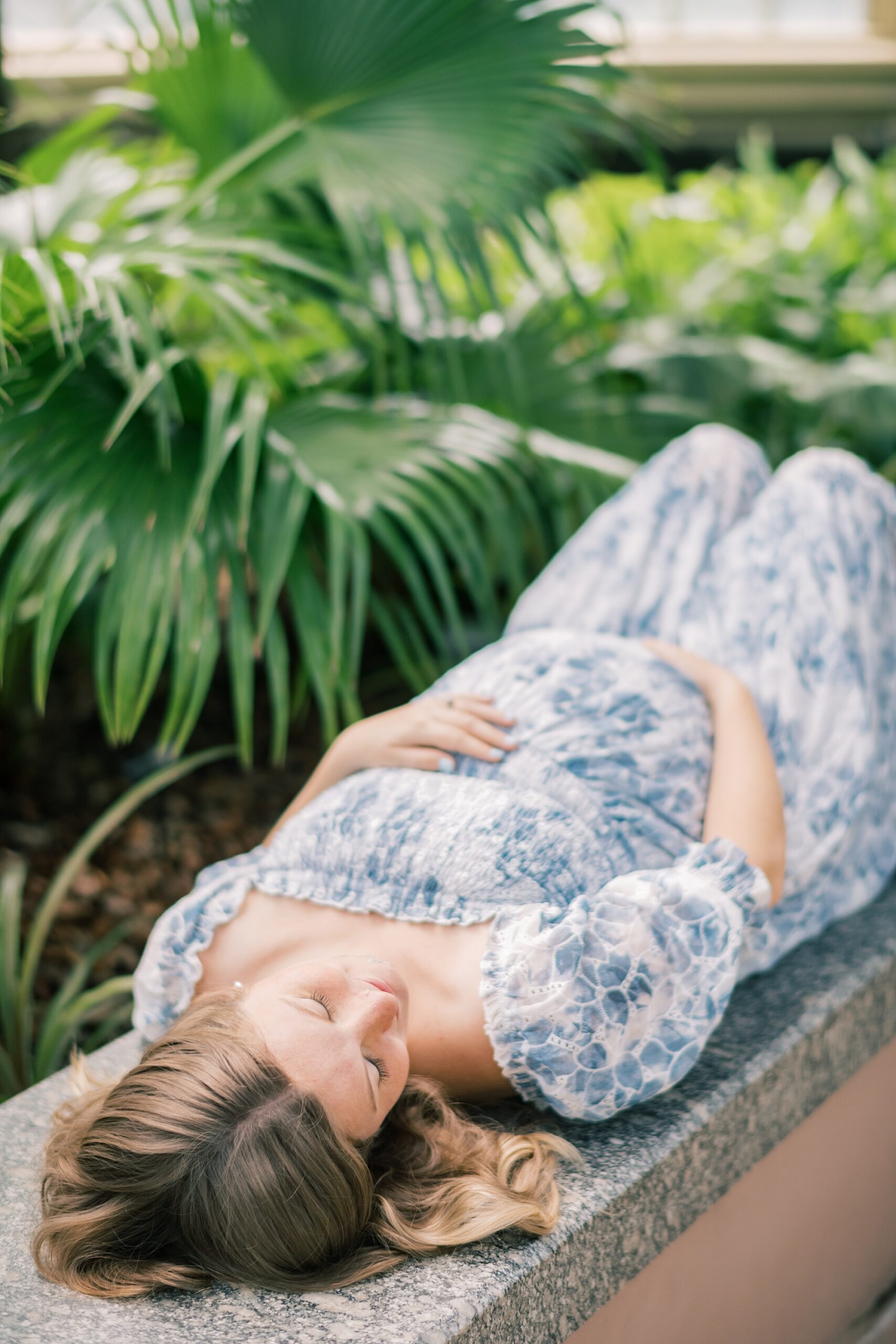 woman lays on bench inside Rawlings Conservatory holding baby bump