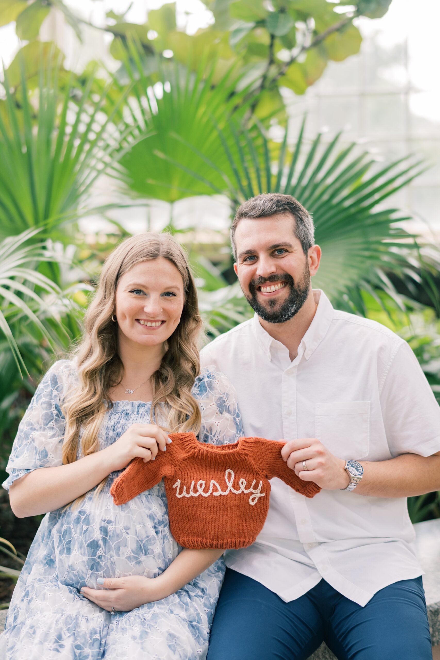 couple sits holding knit sweater between them during Rawlings Conservatory maternity portraits 