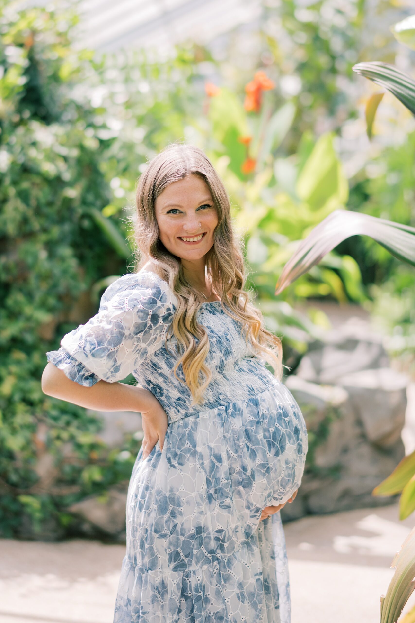 blonde woman holds baby bump in blue and white dress inside Rawlings Conservatory