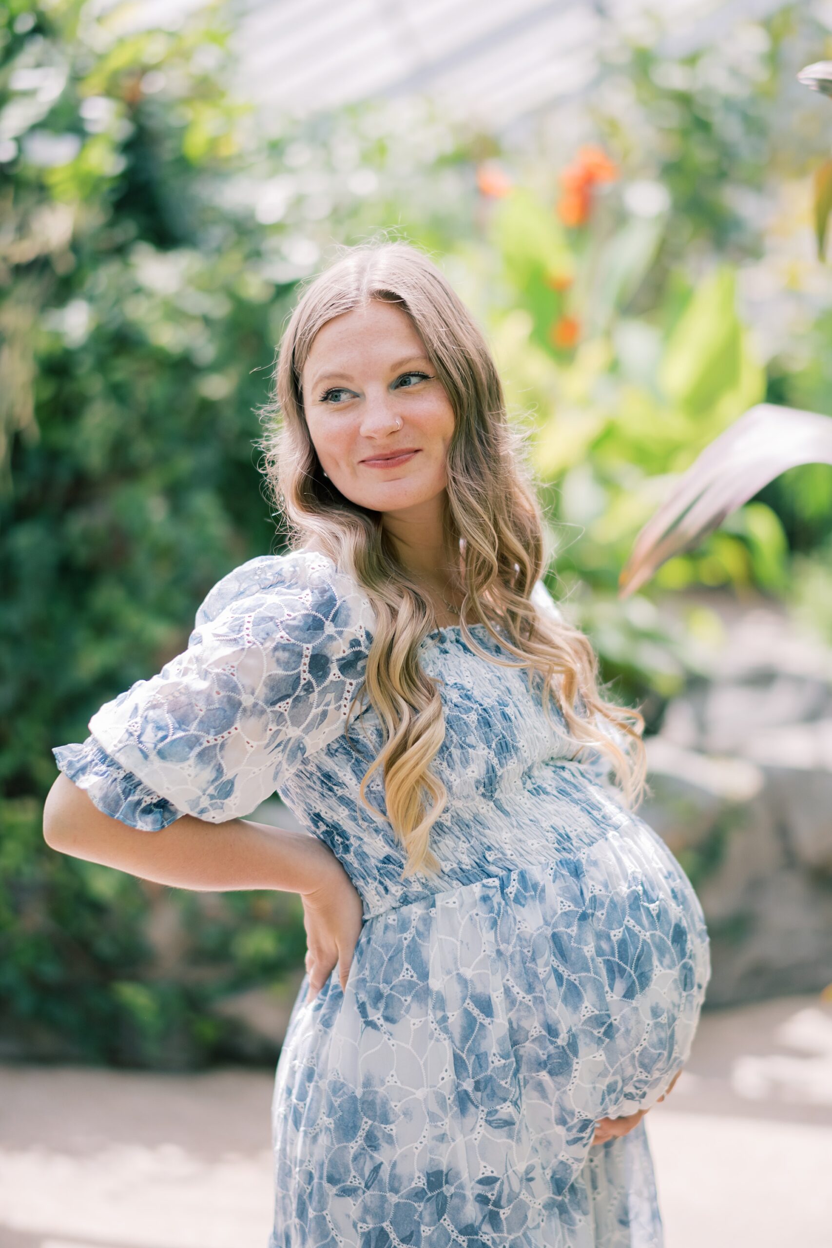 mom holds back showing off baby bump in blue and white dress