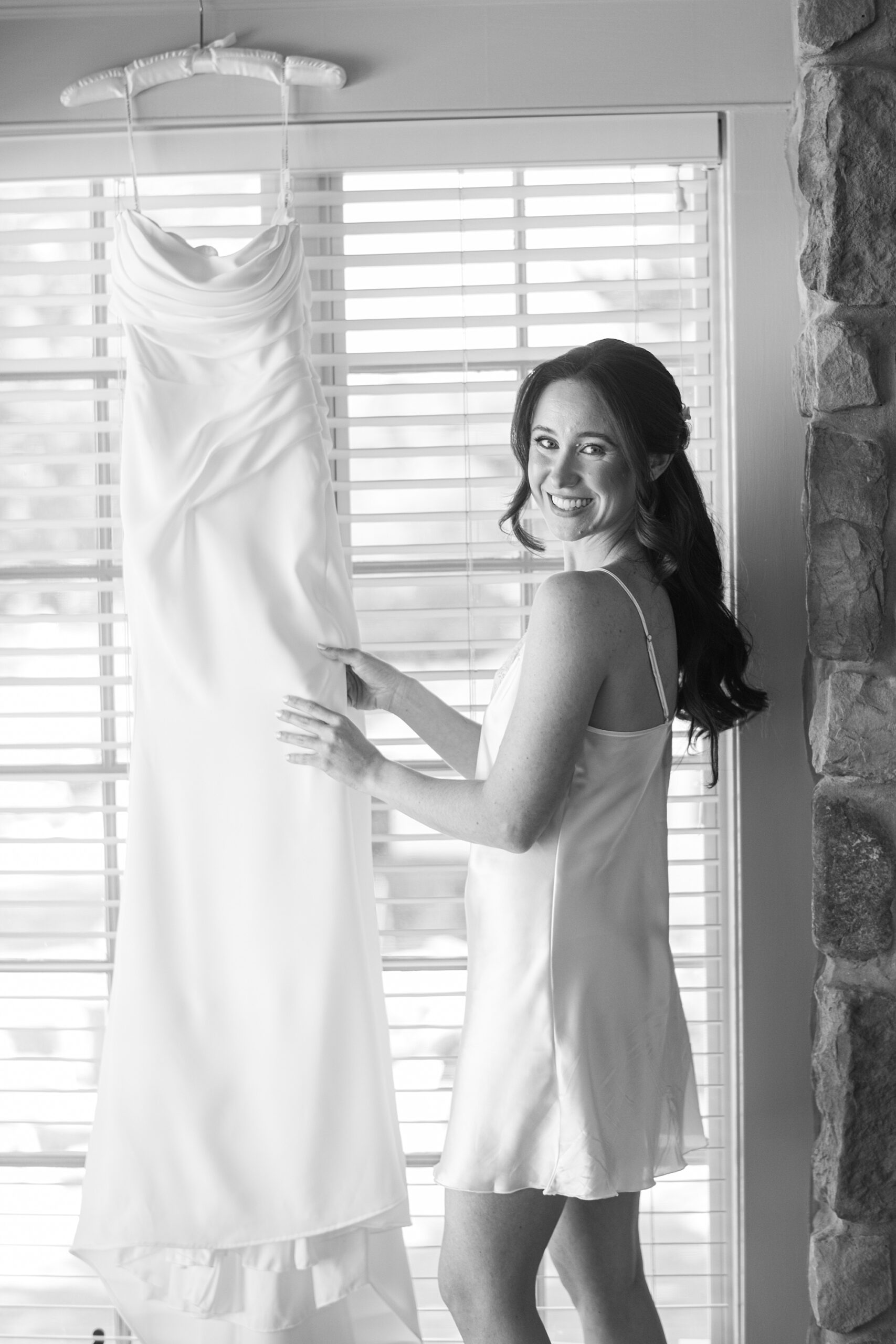 bride looks at wedding dress hanging in window