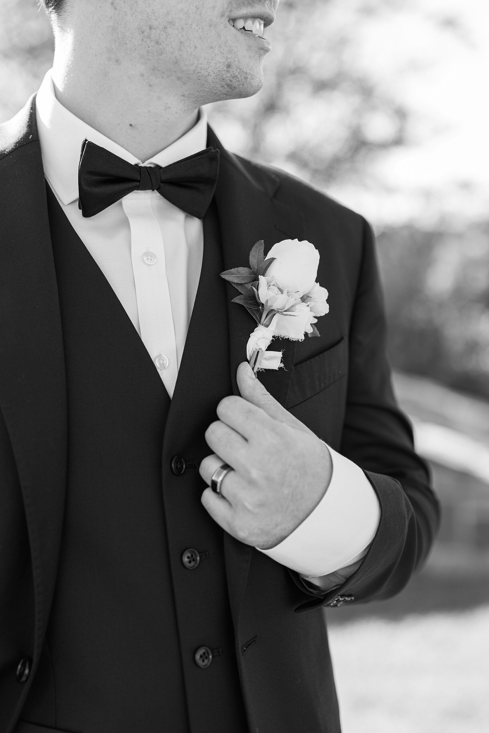 groom holds lapel of suit jacket showing off white boutonnière 