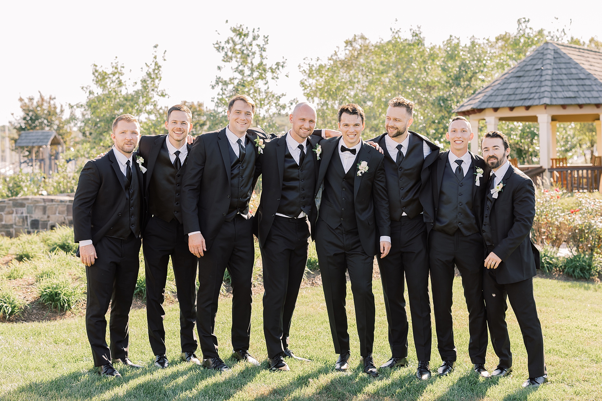 groom stands with groomsmen in black suits at Herrington on the Bay