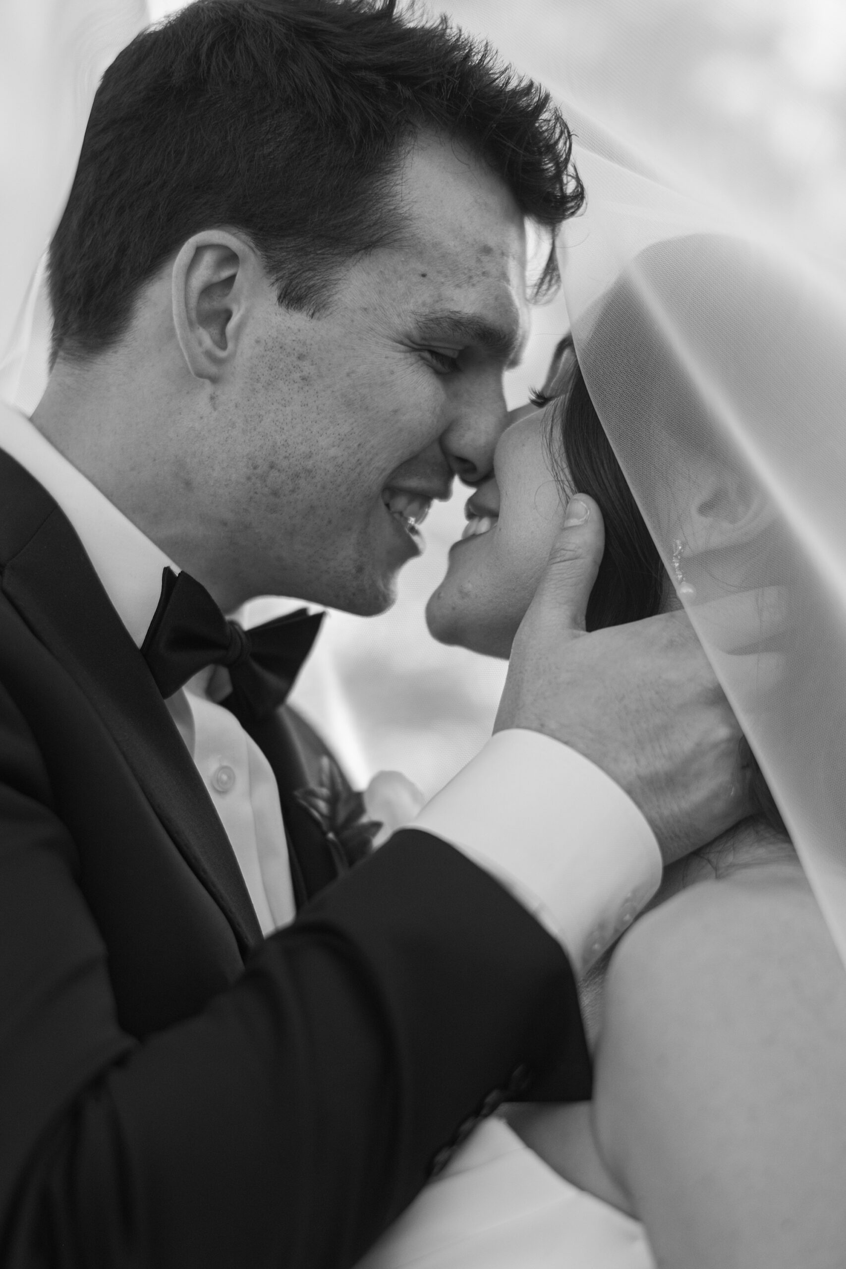 newlyweds lean together under bride's veil for a kiss