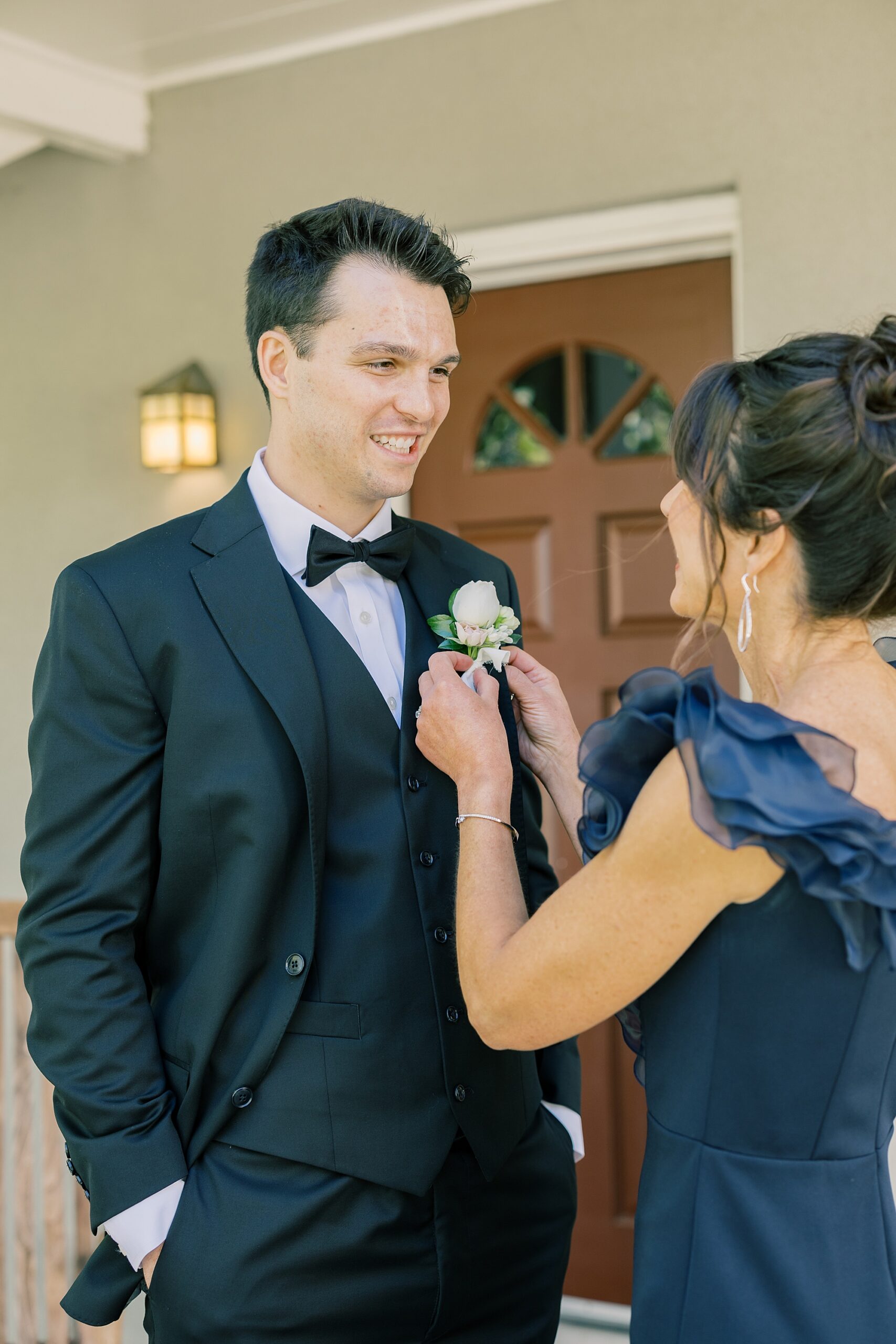 mother helps groom with white boutonnière on suit lapel