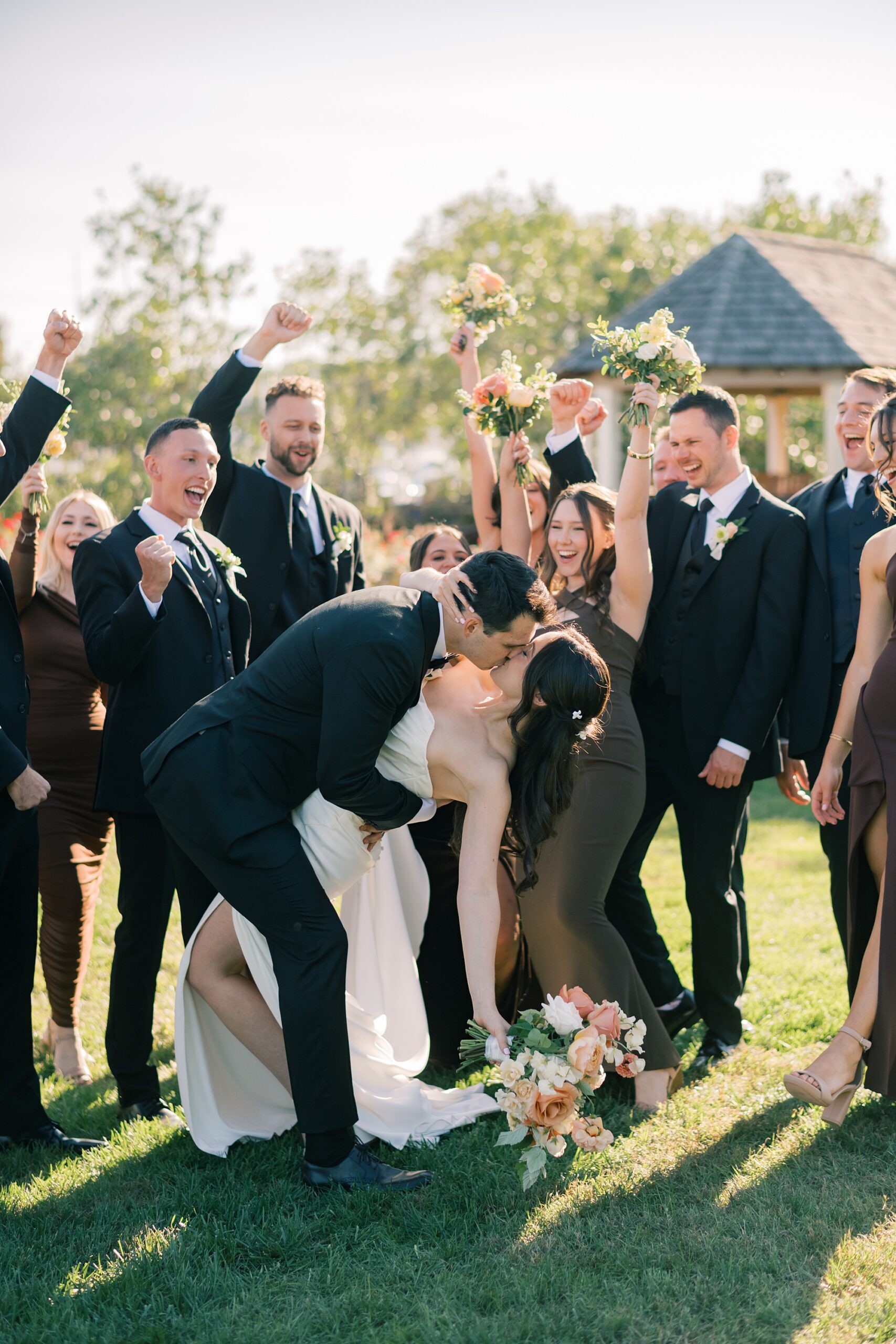 newlyweds kiss while bridal party in fall colors cheers them on