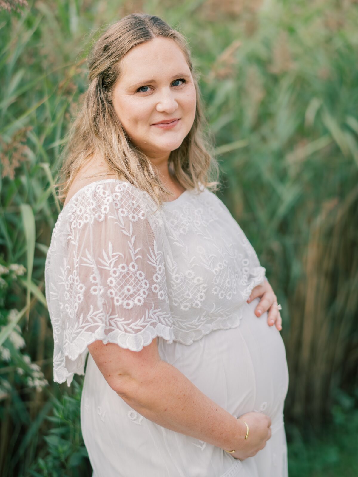 expecting mother poses holding baby bump in white linen dress during maternity session in Annapolis Maryland