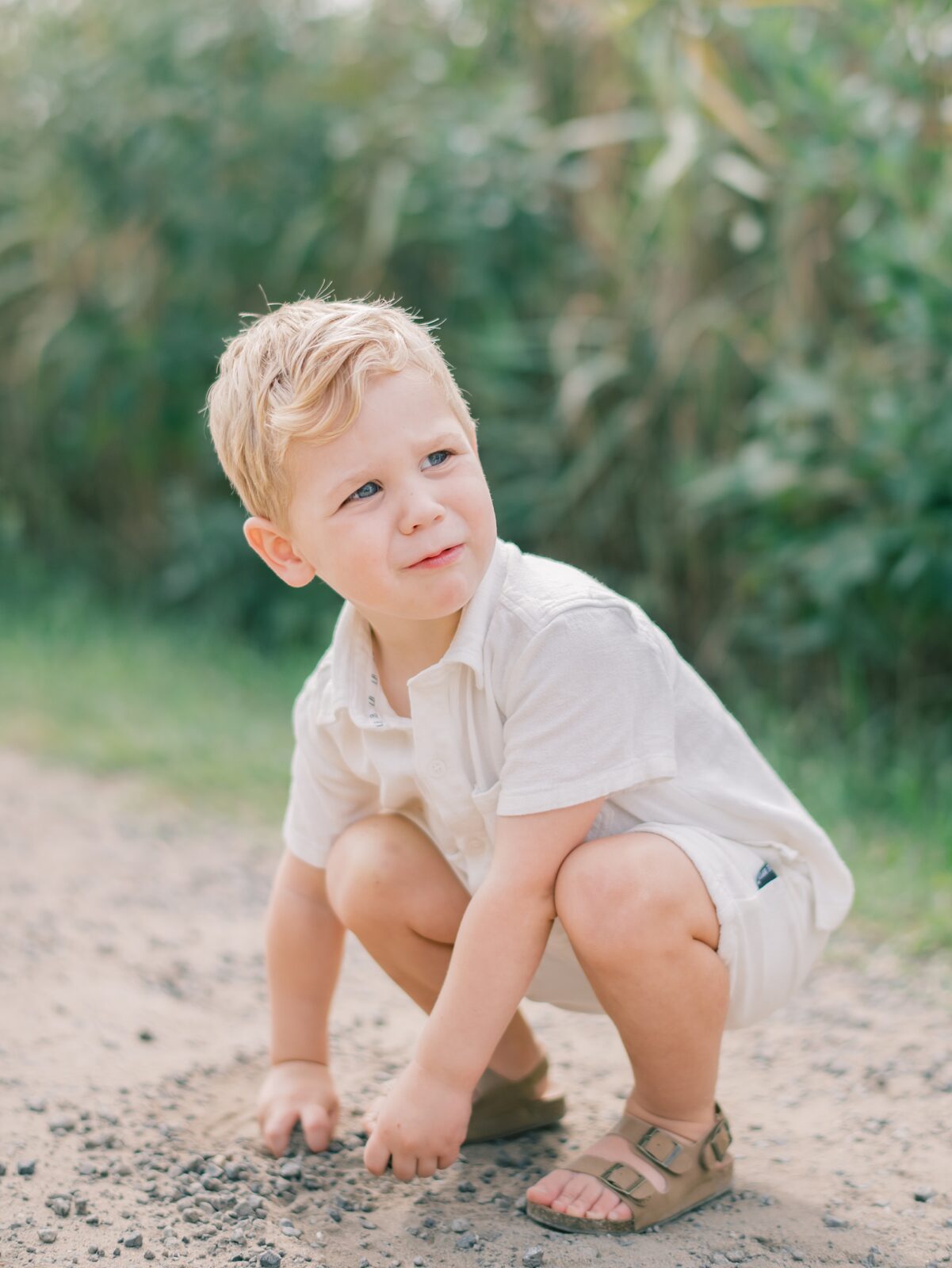 toddler in white linen outfit plays in the sand