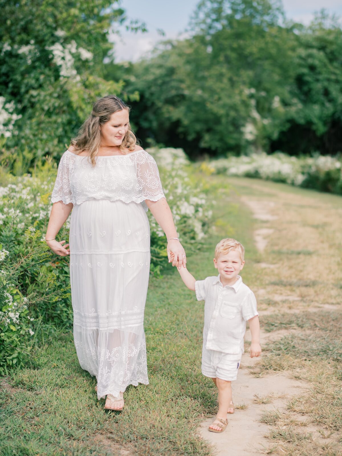 mom holds son's hand walking through park during maternity session in Annapolis Maryland