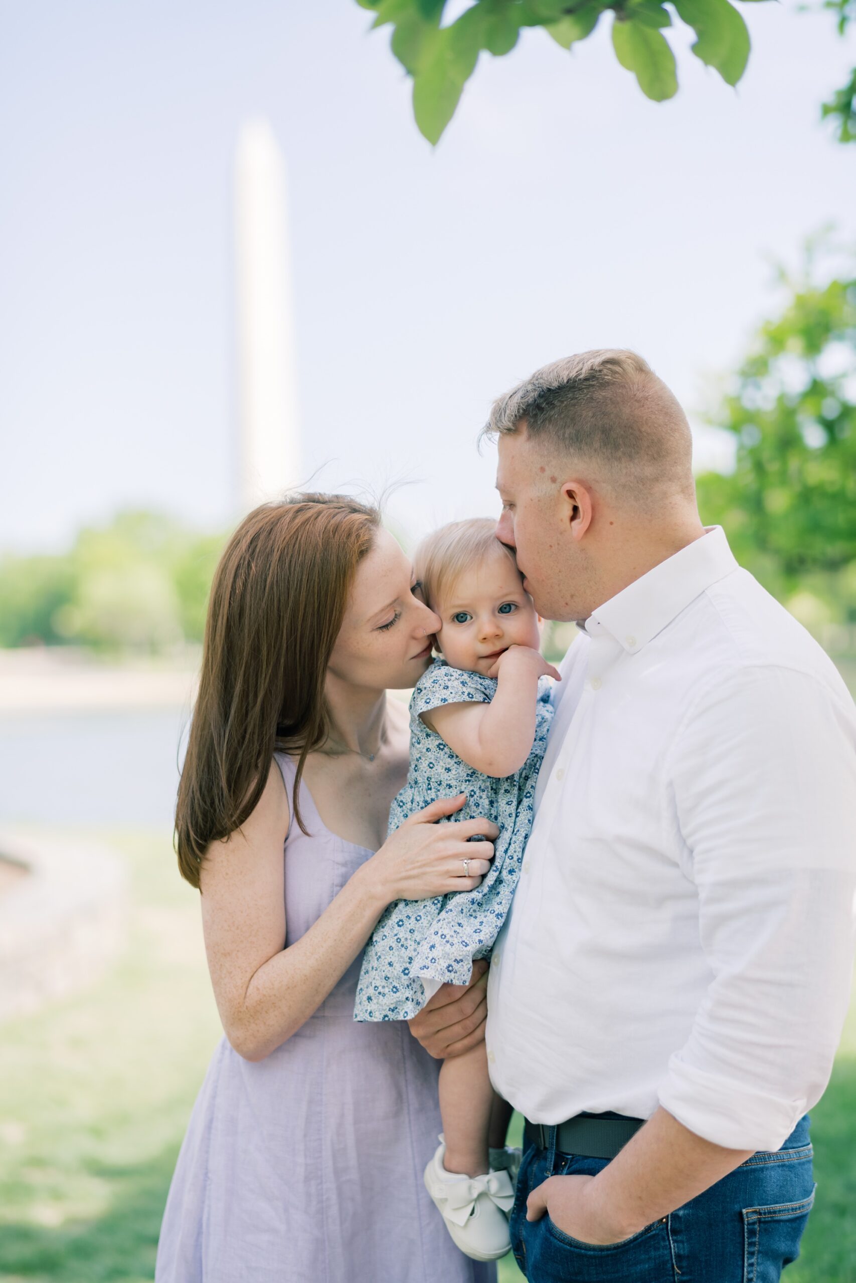 parents lean to kiss toddler leaning against dad's chest