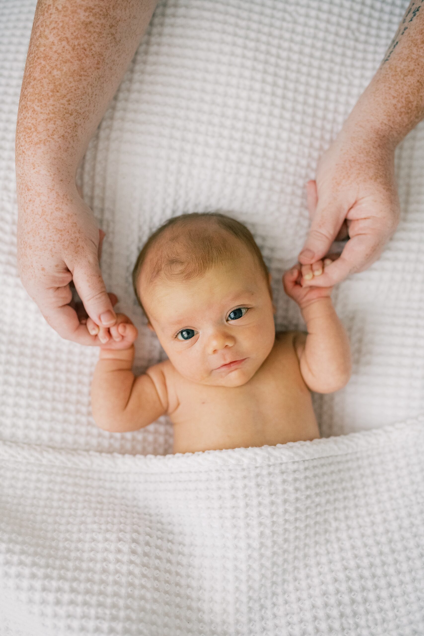 mom holds baby's hands laying in blanket