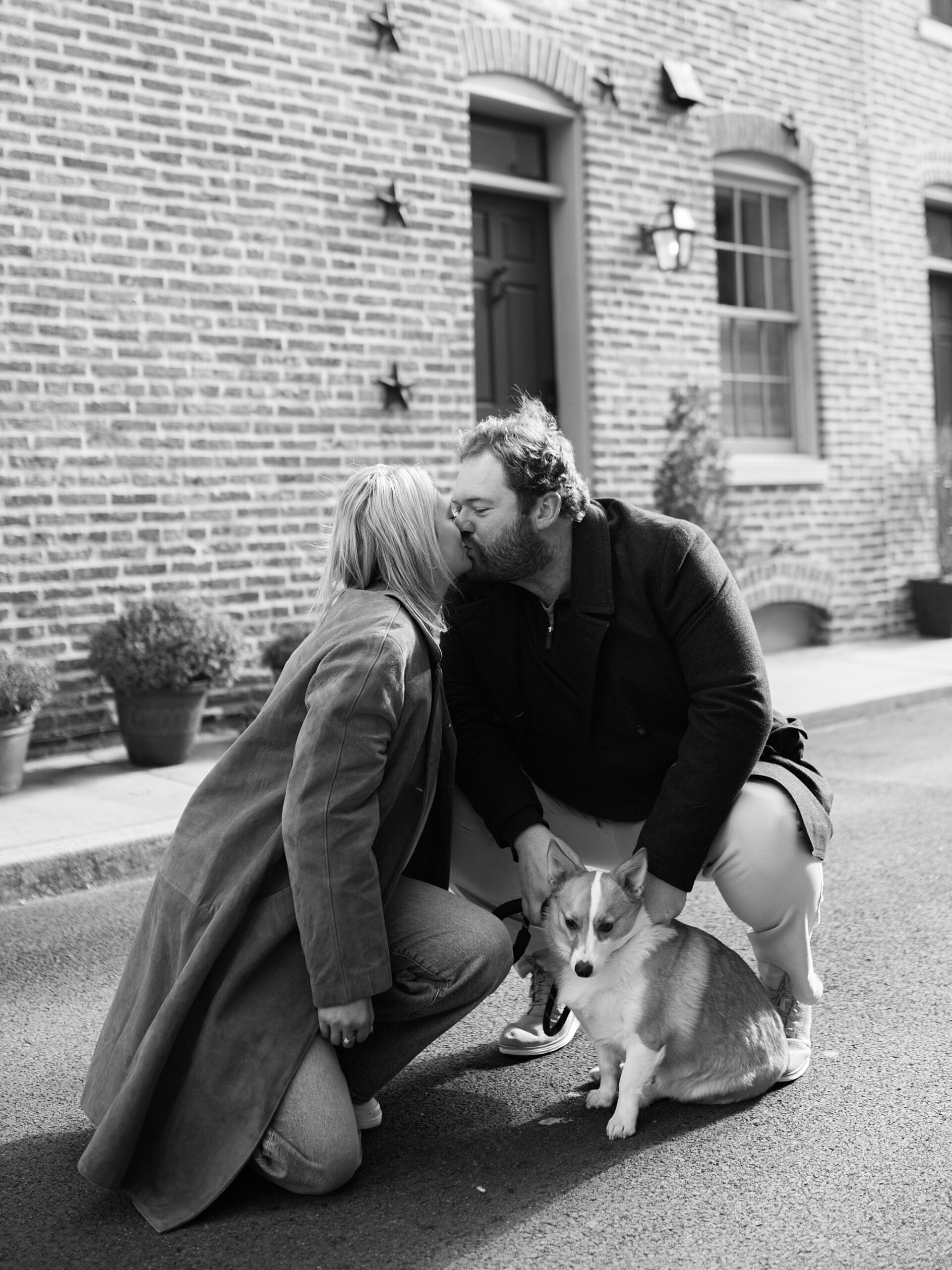 engaged couple kiss in Fells Point neighborhood while holding dog between them 