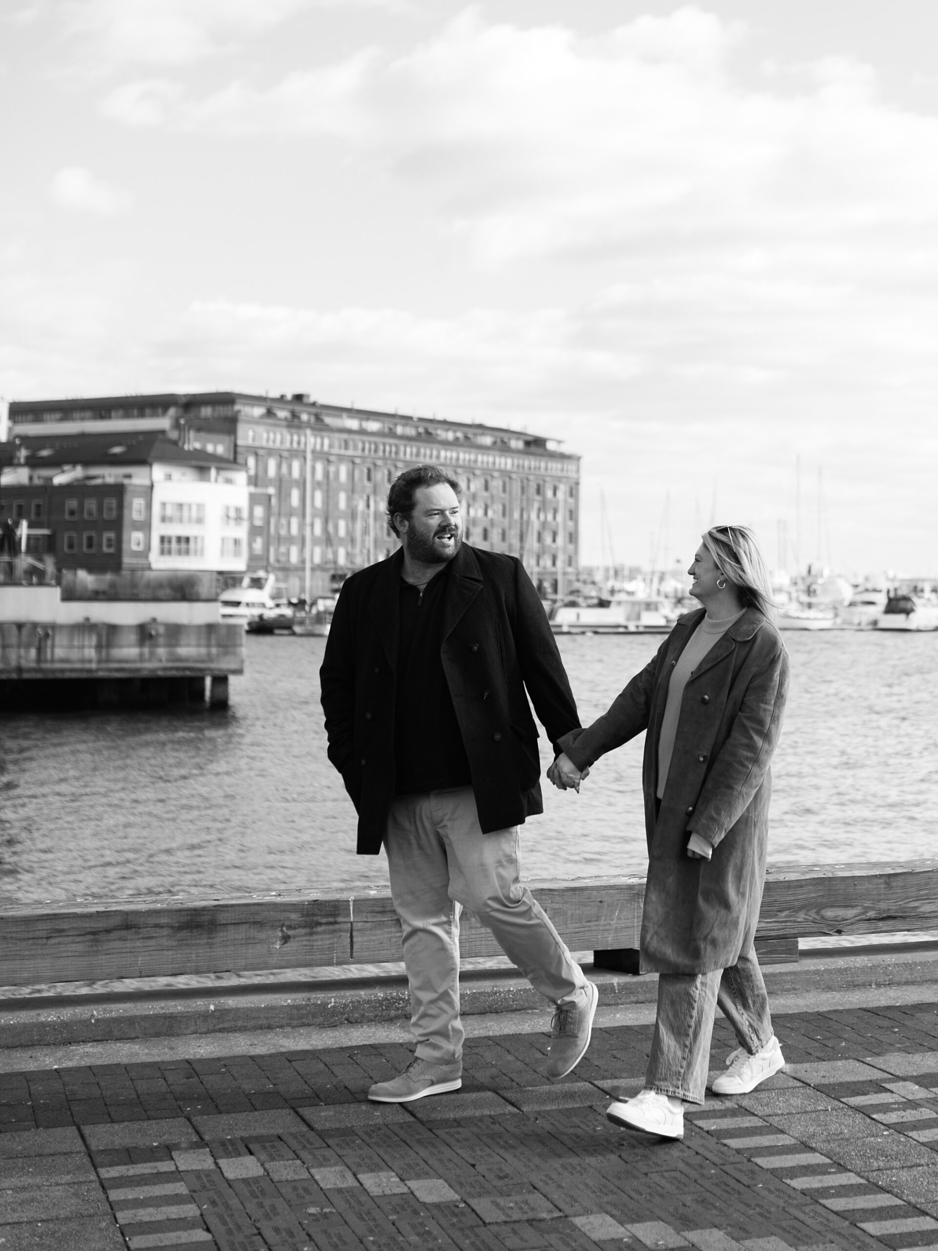 man and woman hold hands walking along Baltimore waterfront 