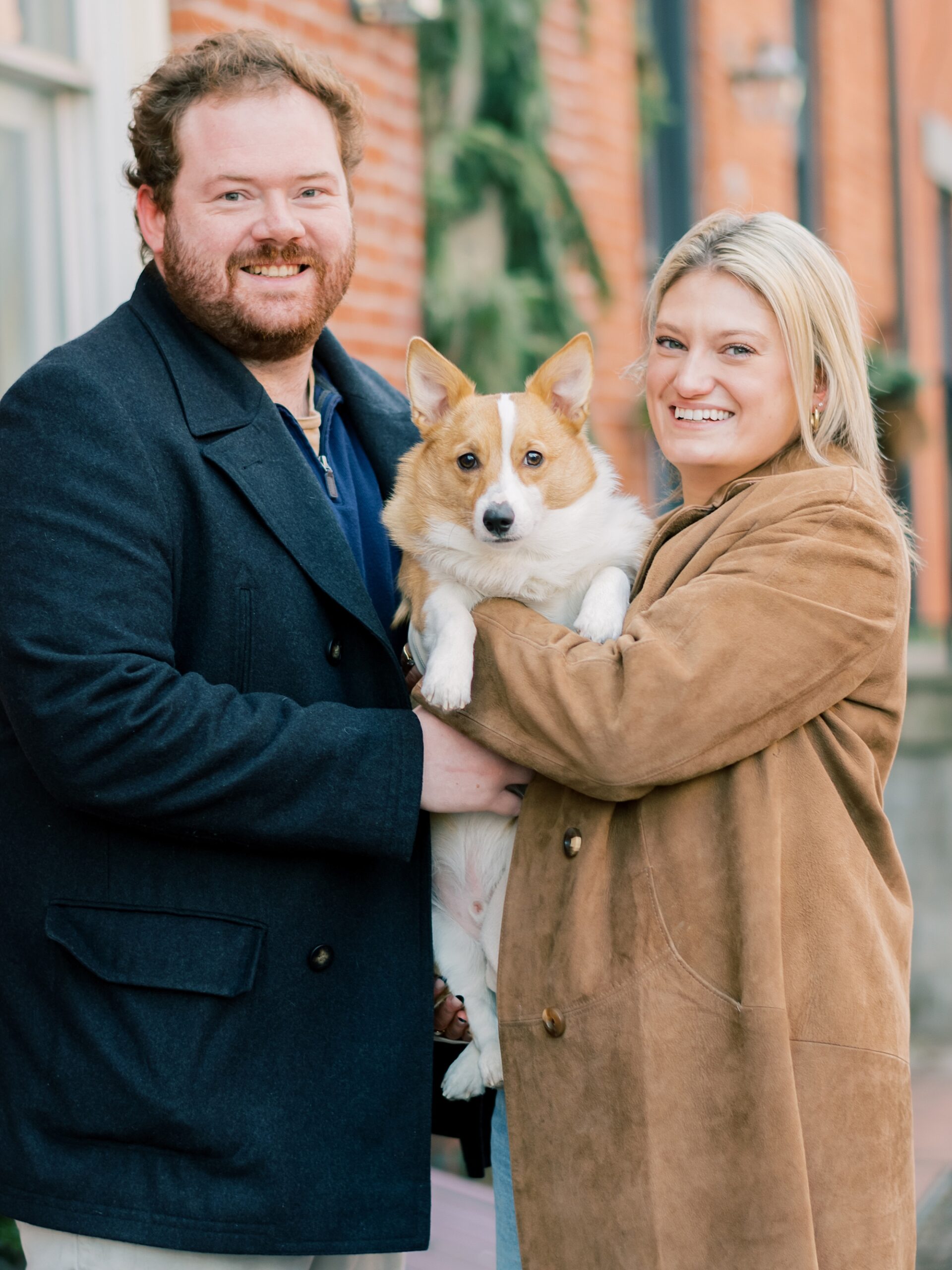 engaged couple hugs corgi between them on street in Baltimore MD