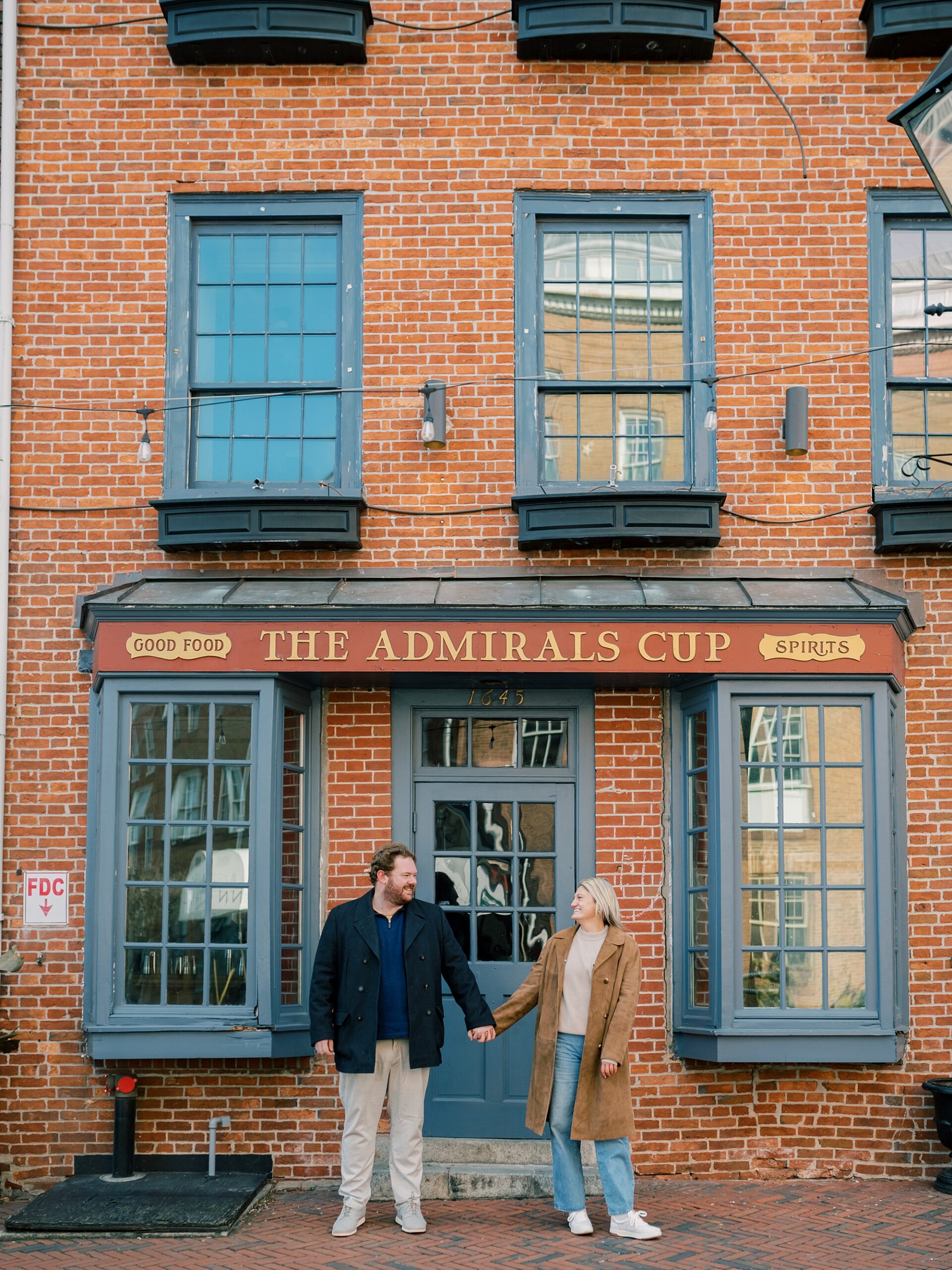 engaged couple holds hands in front of brick building during Baltimore engagement session