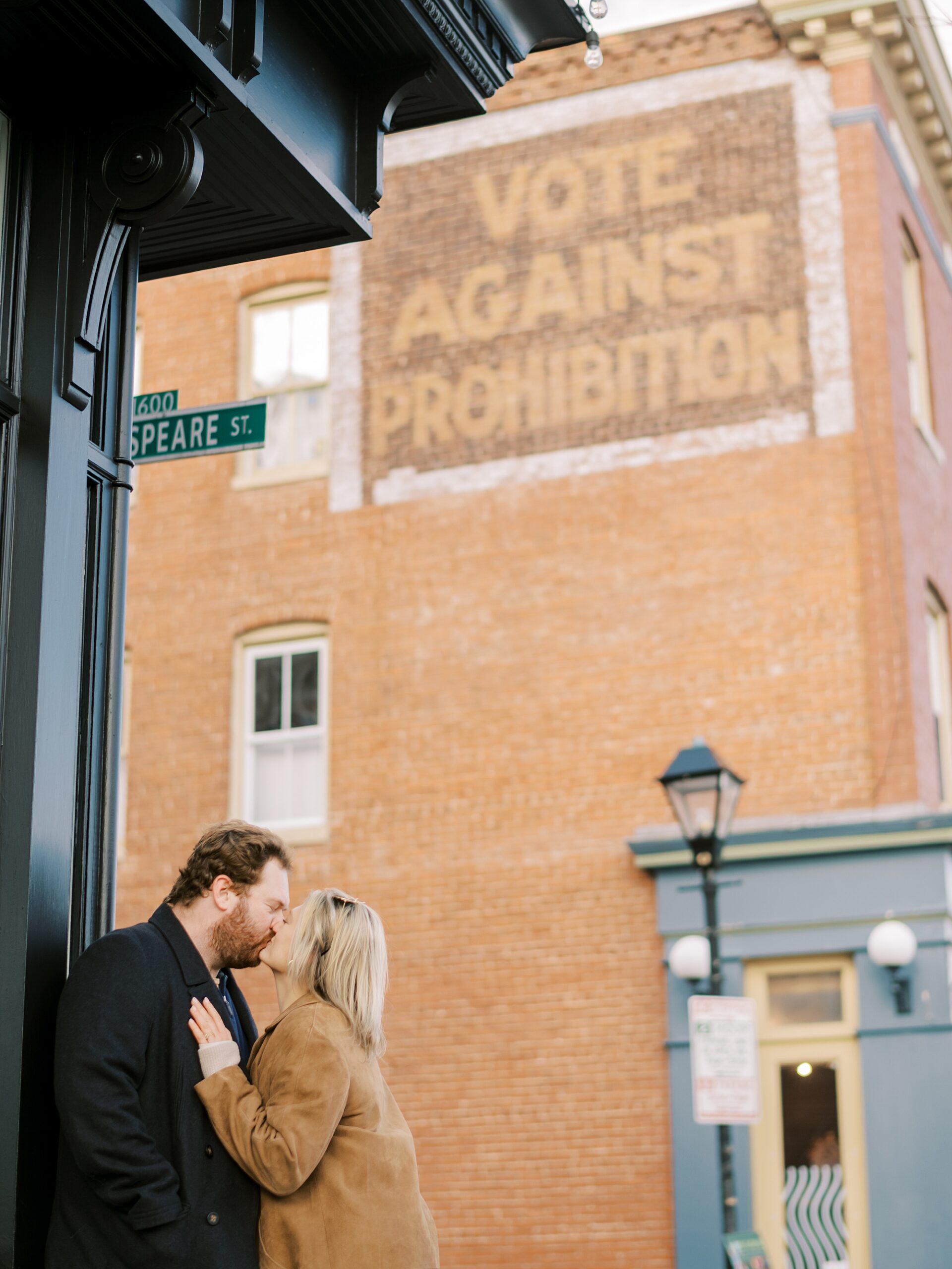 woman leans into man kissing him in front of brick building 