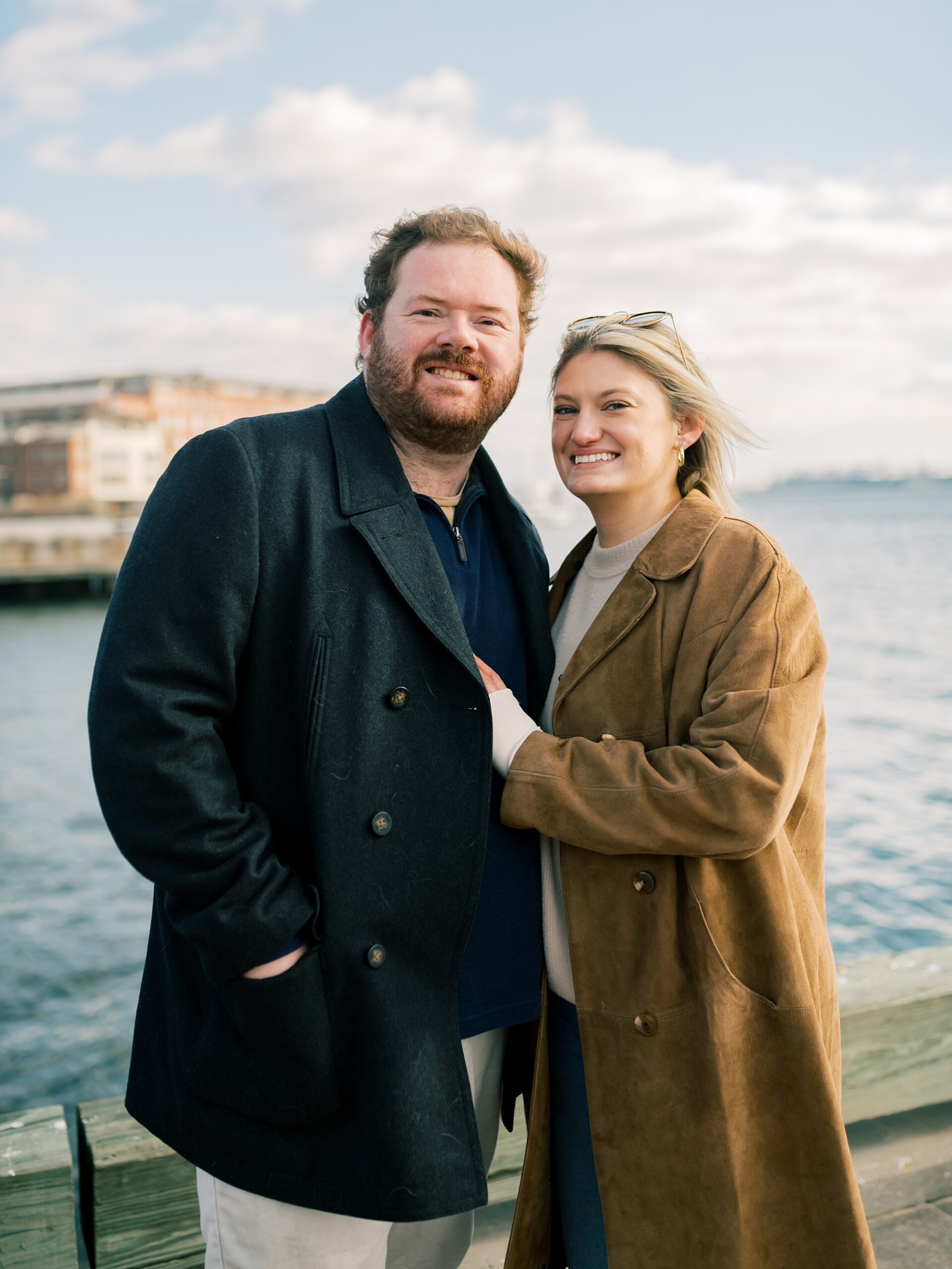 engaged couple hugs in front of waterfront during Baltimore engagement session