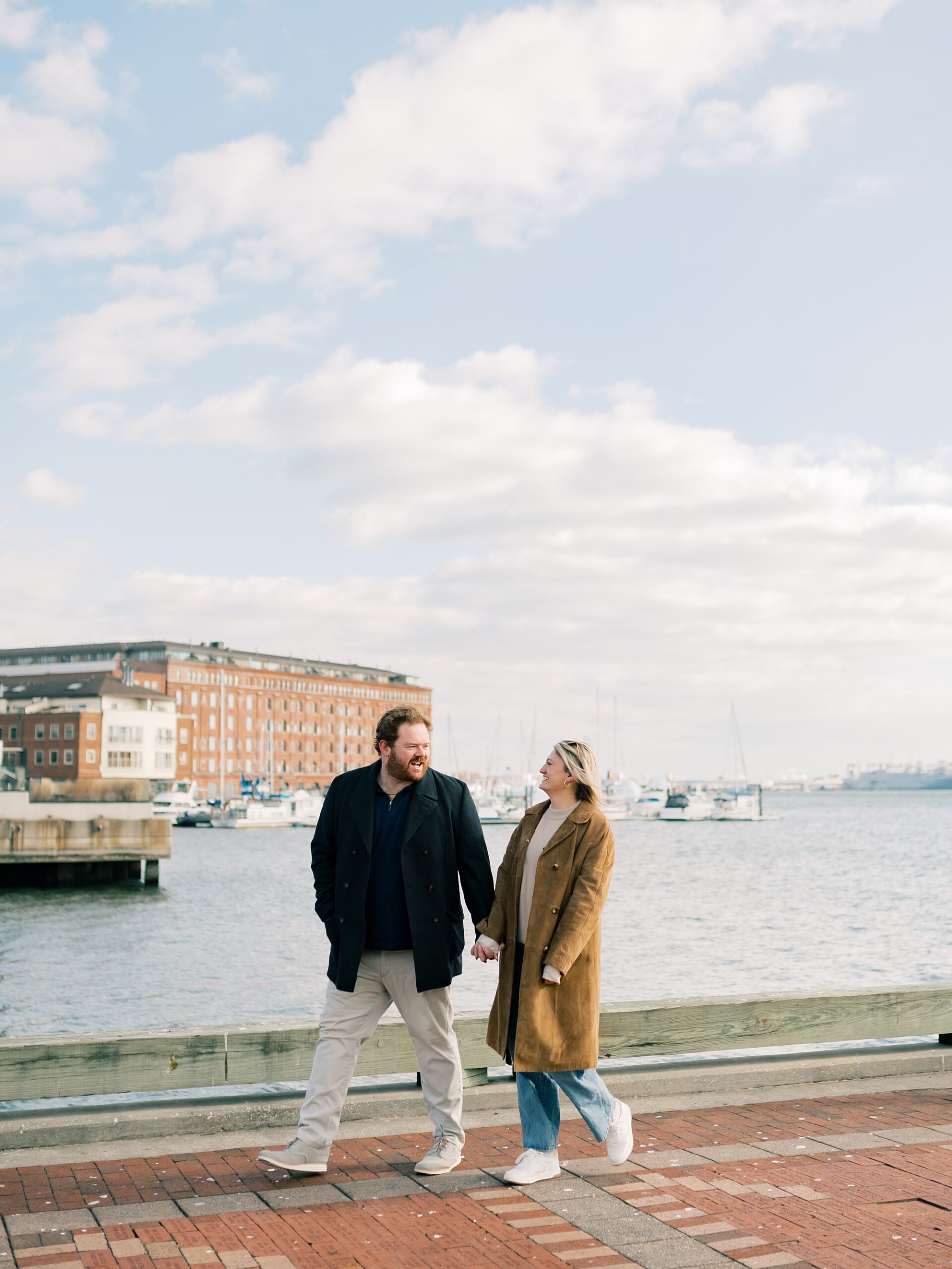 couple walks along waterfront during Baltimore engagement session