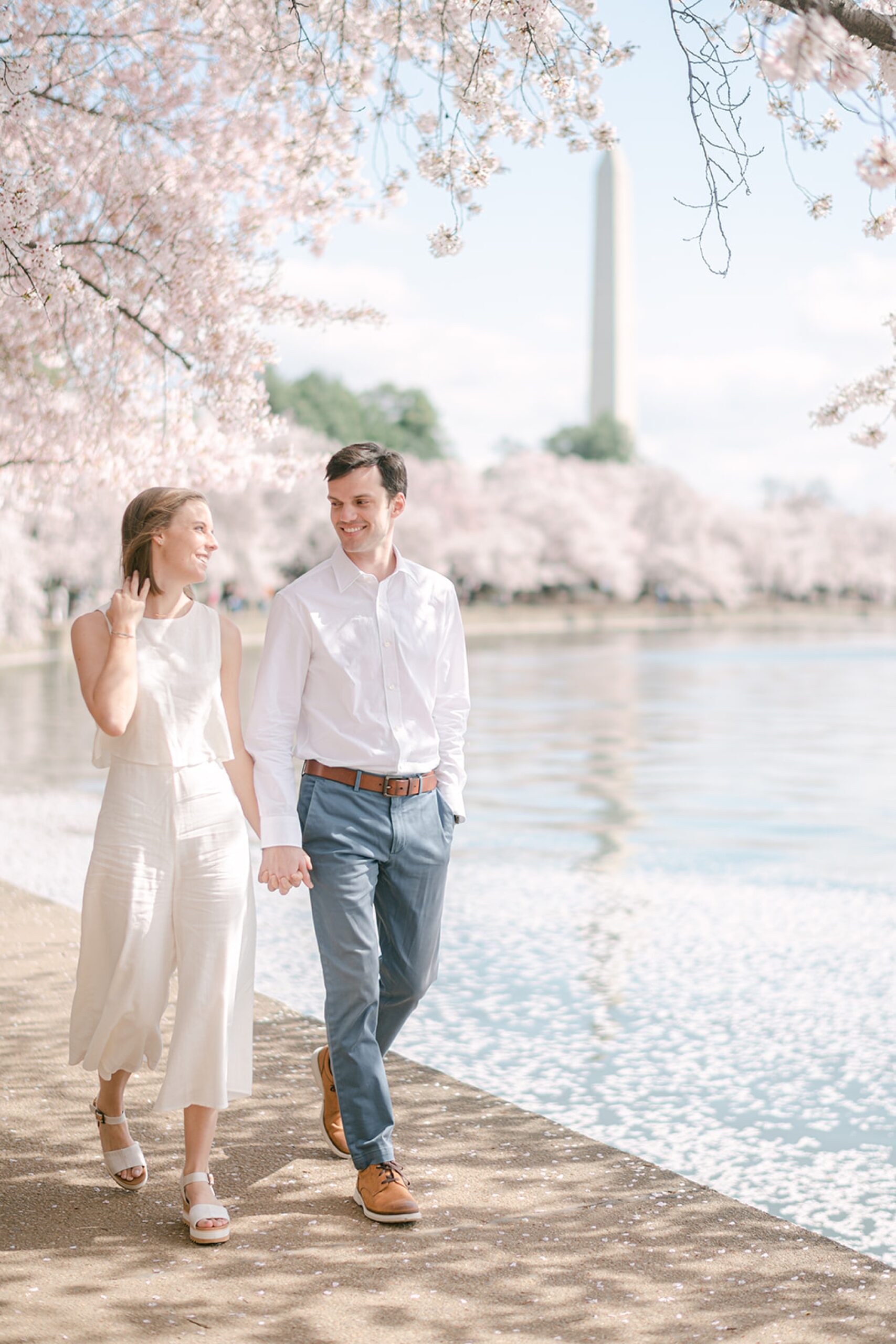 couple holds hands walking under cherry blossoms in Washington DC