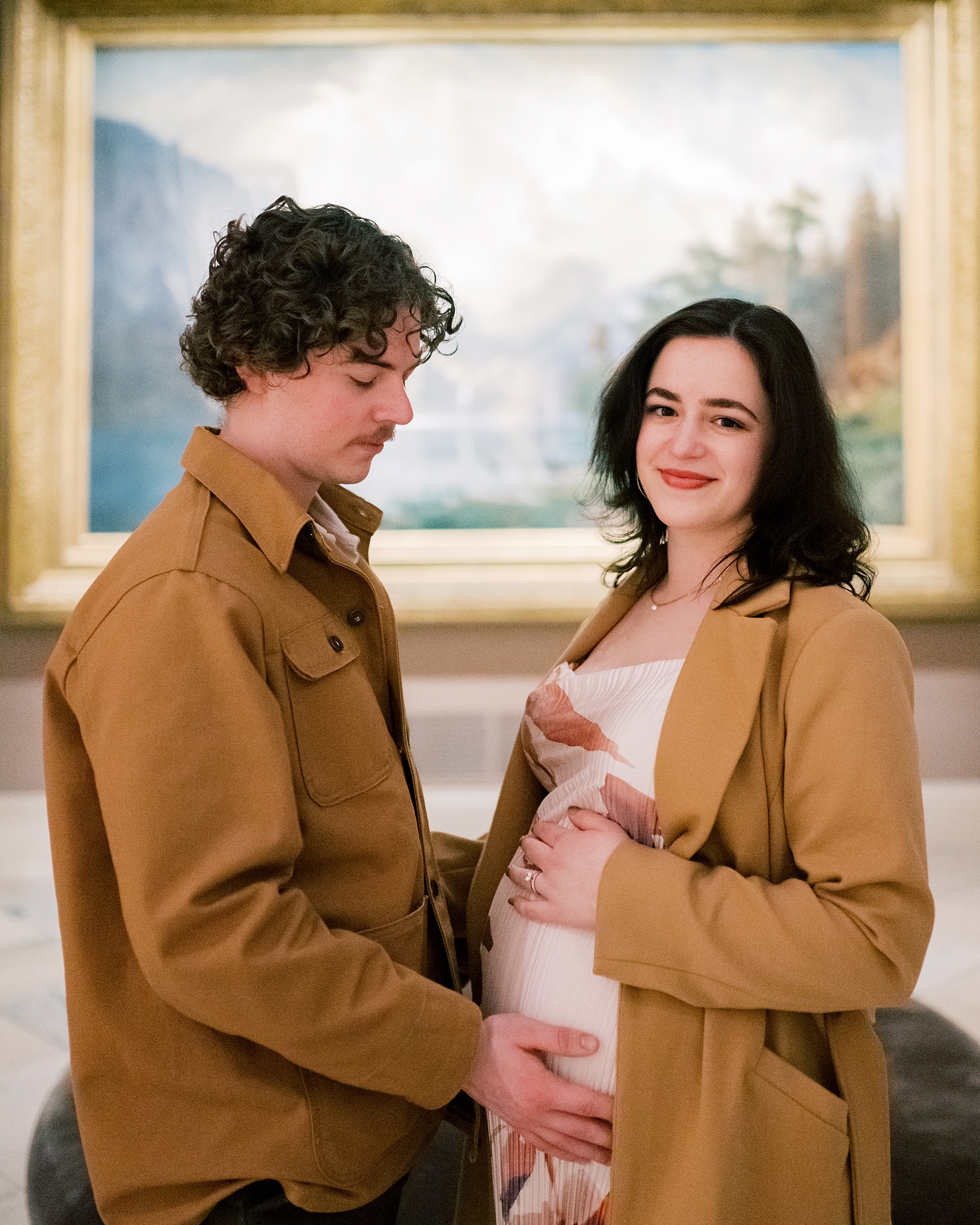 man holds woman's baby bump smiling at her during maternity session
