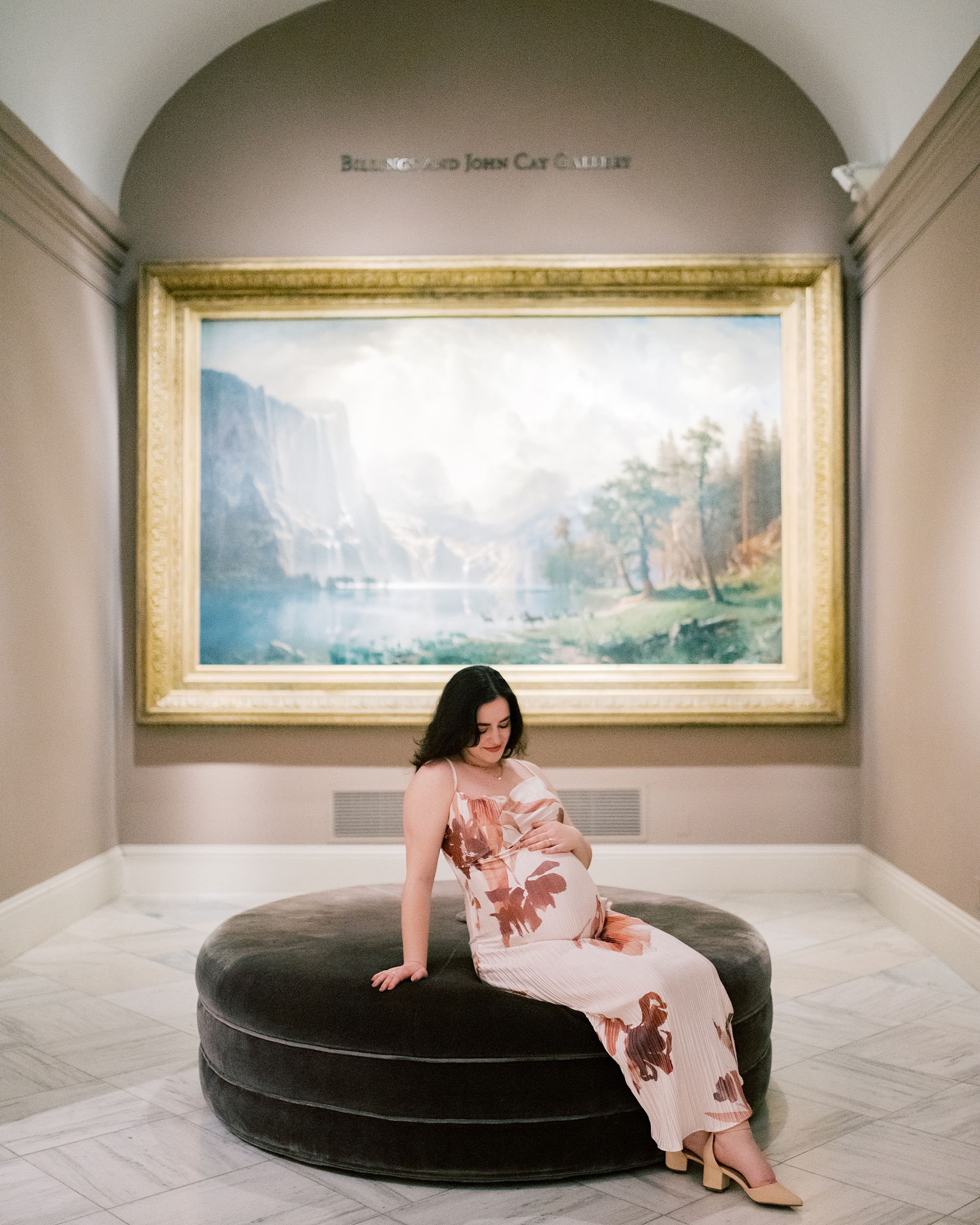 expecting mother holds baby bump sitting in front of a painting inside the National Portrait Gallery